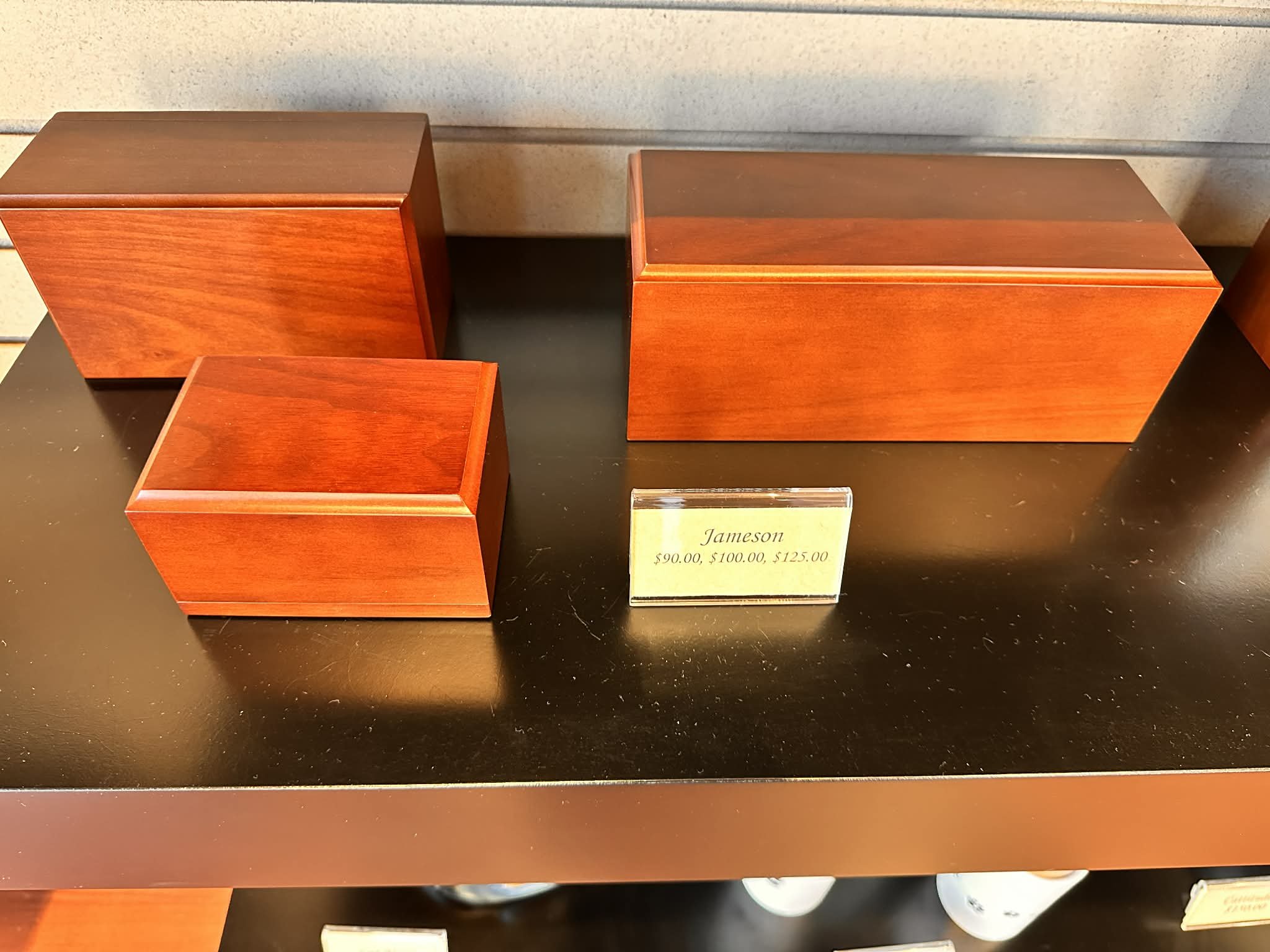 Three wooden jewelry boxes with a reddish finish, displayed on a black surface, with a yellow price tag indicating prices of $90.00, $100.00, and $125.00.