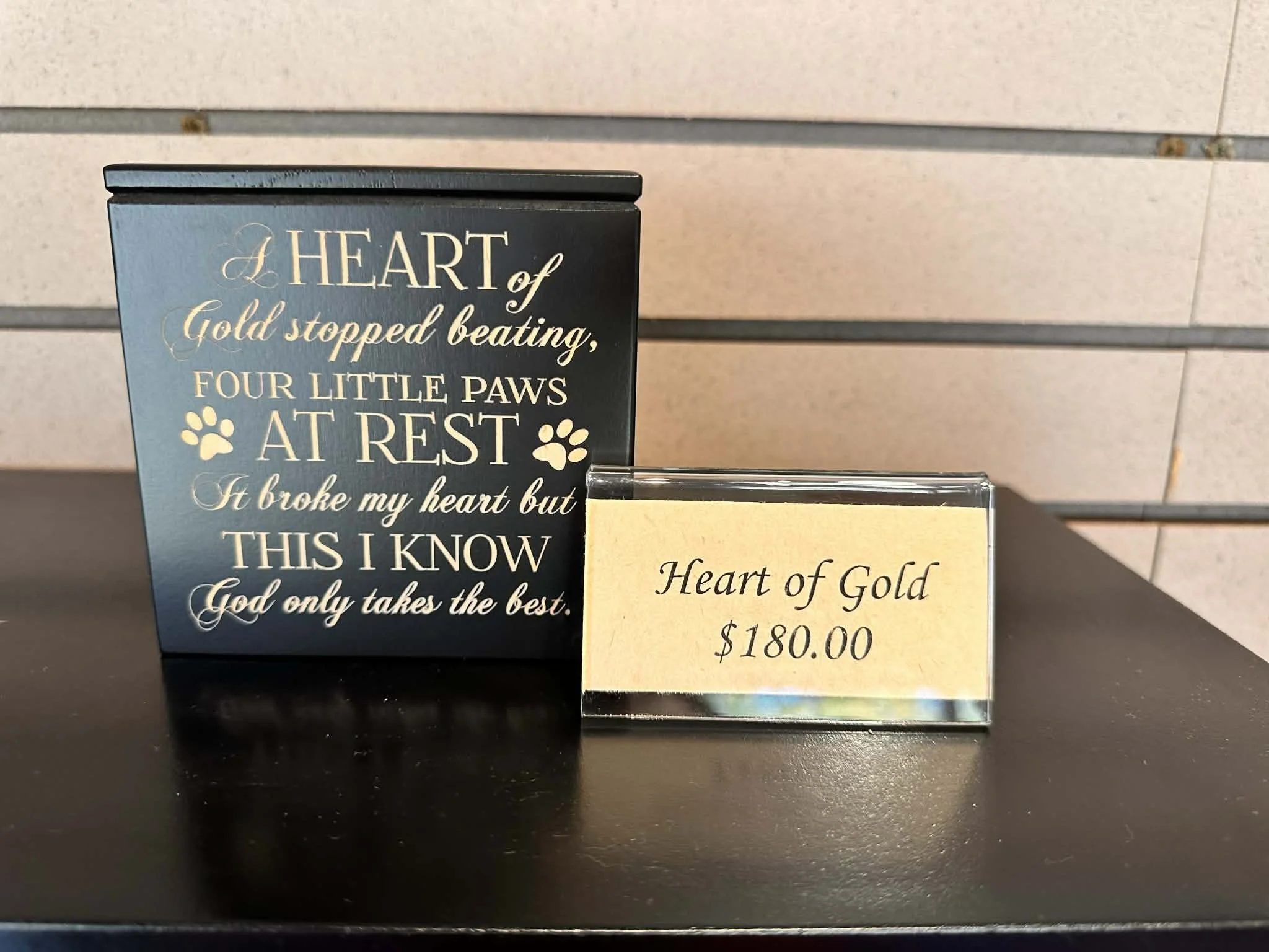 Close-up of a black and gold sign with a sentimental message about love and heartache, placed in front of a beige tiled wall.