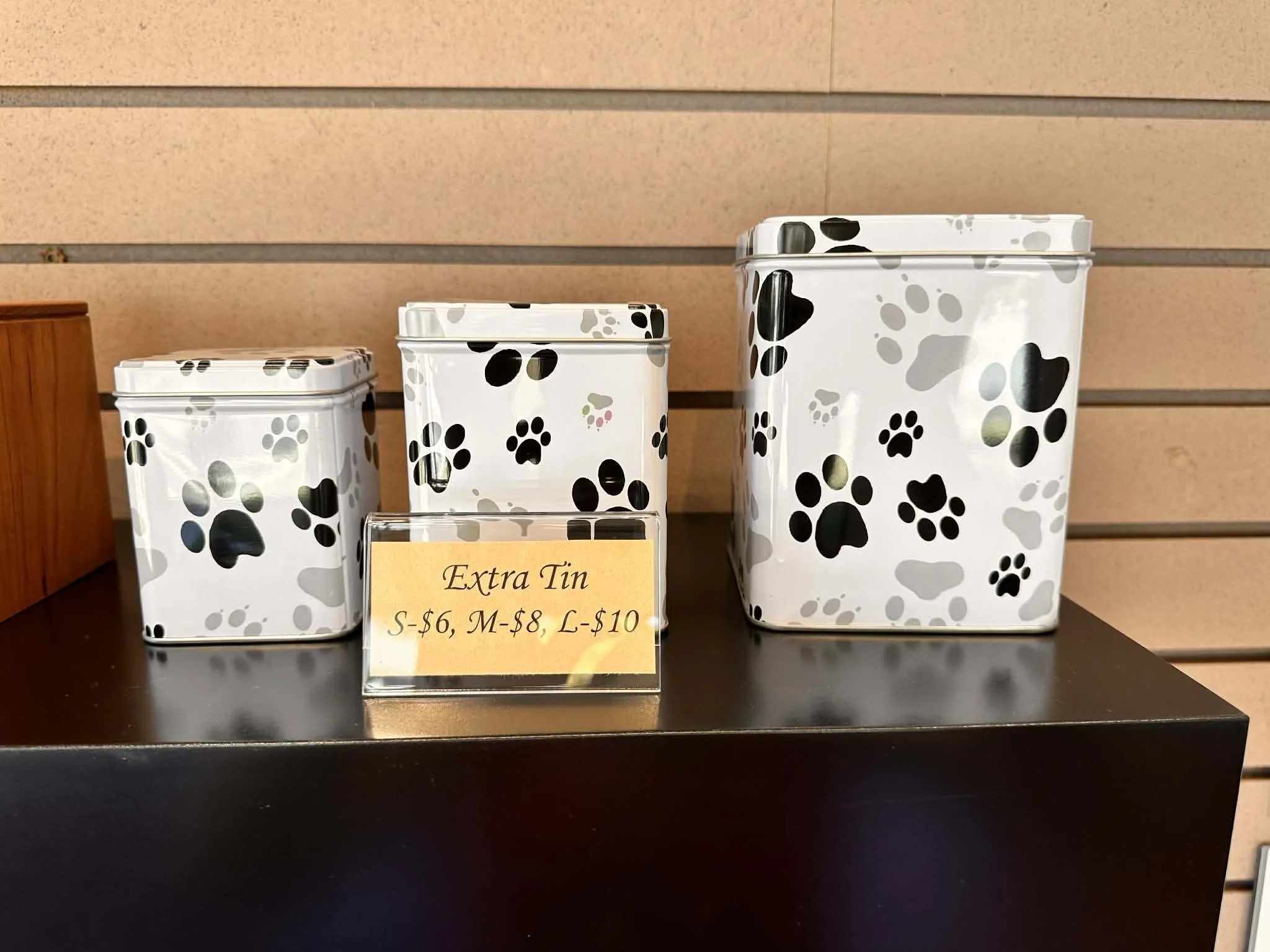 Three white containers with black and gray paw print patterns, displayed on a black surface next to a yellow price sign.