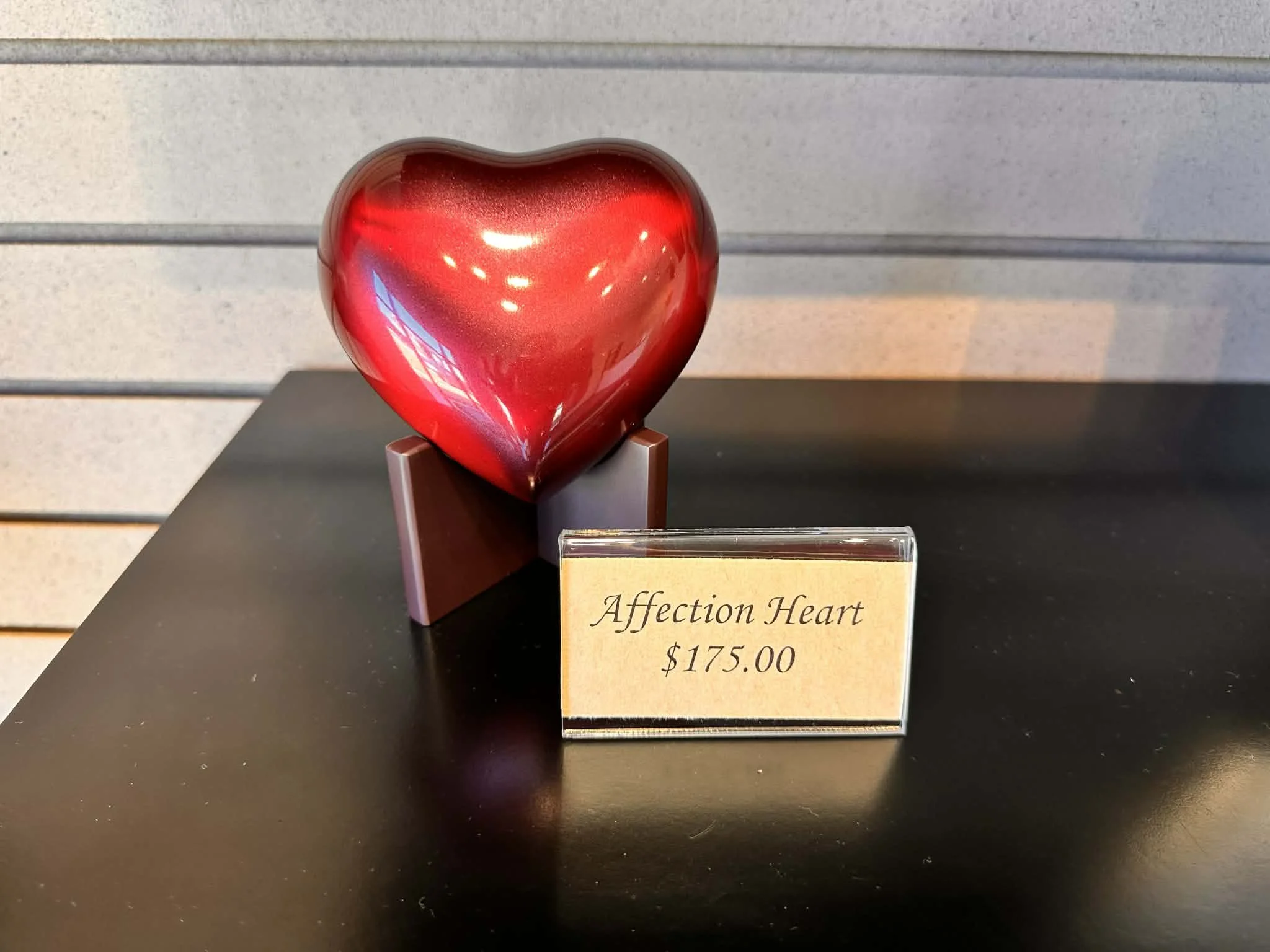 A metallic red heart-shaped sculpture displayed on a stand inside a store.