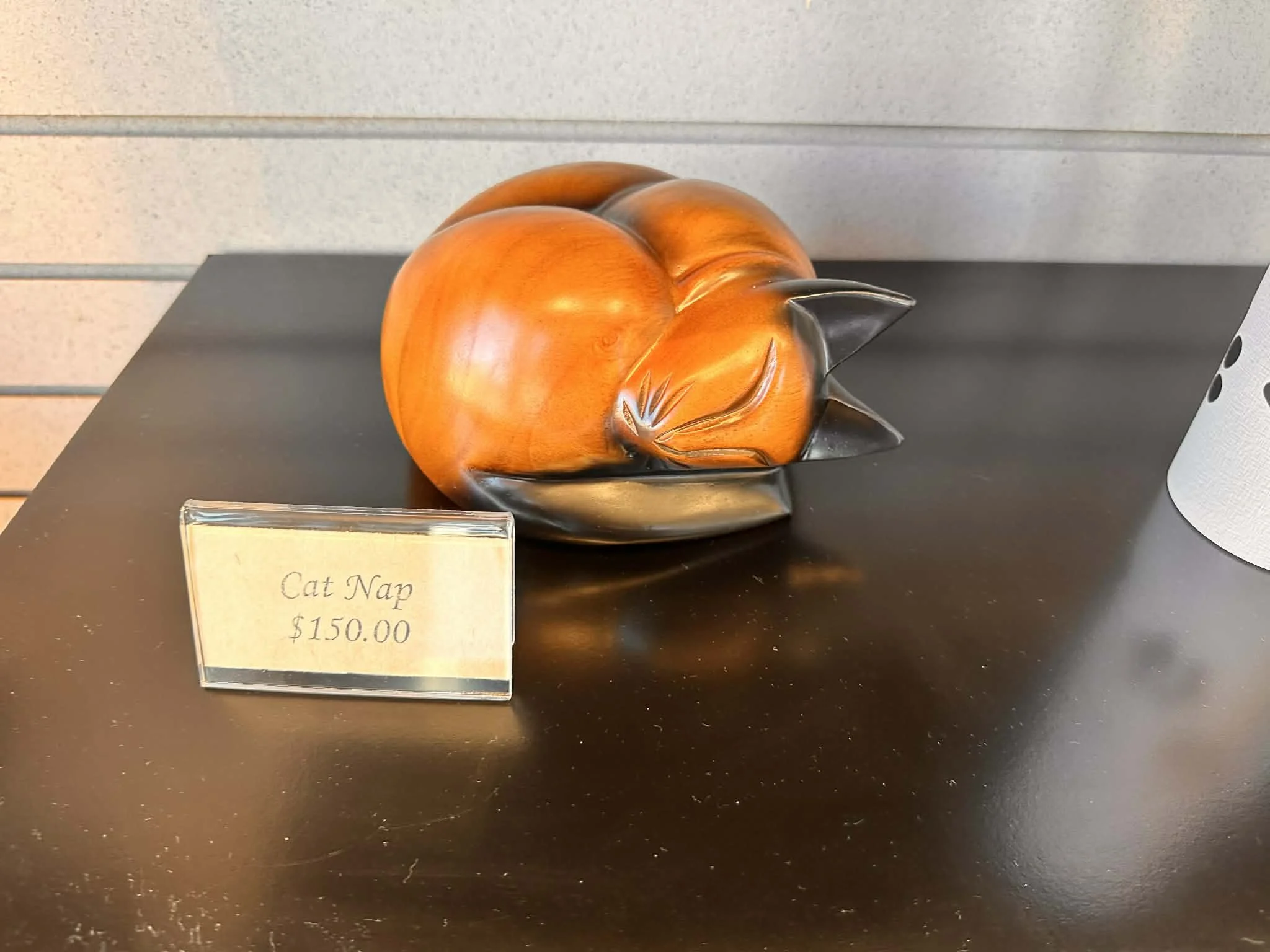 A decorative sculpture of a sleeping cat on display, with a placard labeled 'Cat Nap' and priced at $150.00.