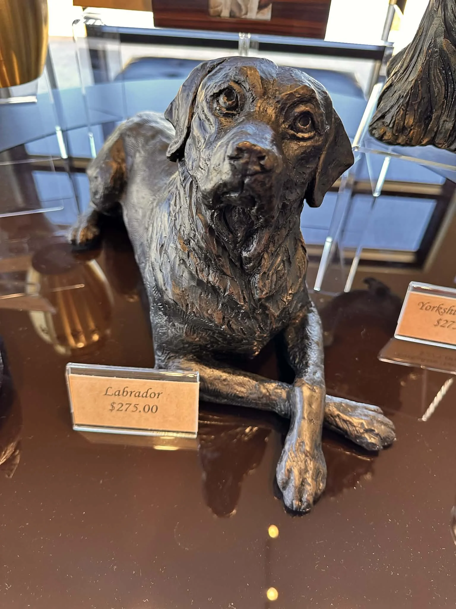 A realistic sculpture of a Labrador dog, sitting on a table, with a price tag of $275.00. The sculpture is detailed with a lifelike expression, textured fur, and a sitting posture.