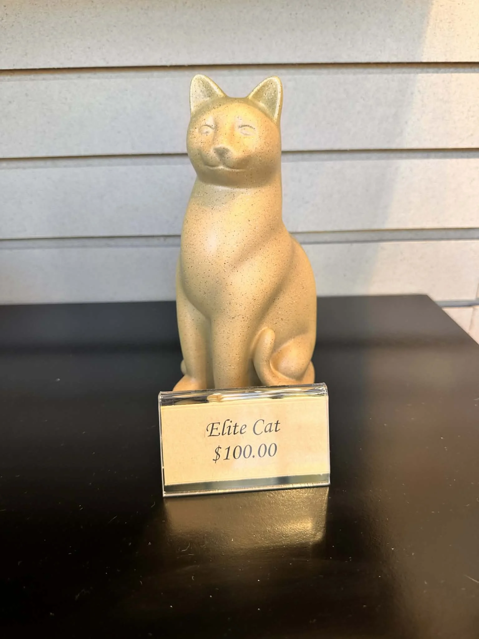 A small sculpture of a cat with a serene expression, labeled 'Elite Cat' priced at $100.00, on display.