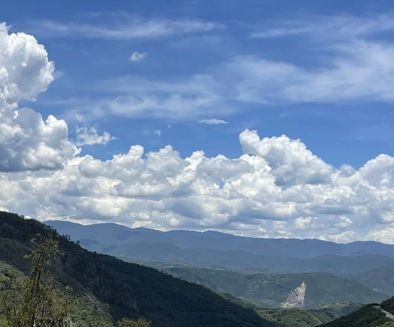 Landscape view of green hills with mountains in the background under a partly cloudy blue sky.