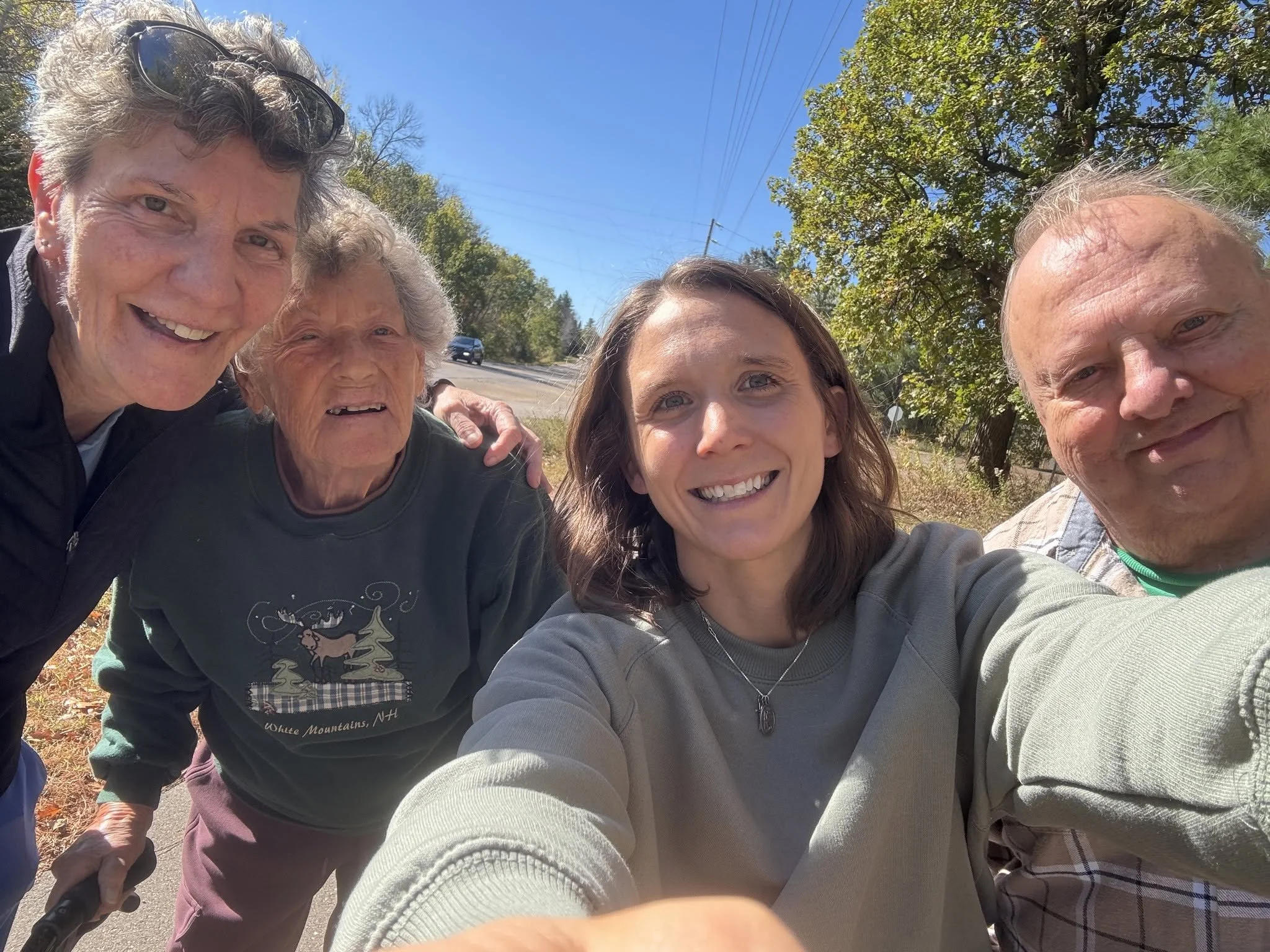 Group of five people taking a selfie outdoors on a sunny day, with trees and power lines in the background.