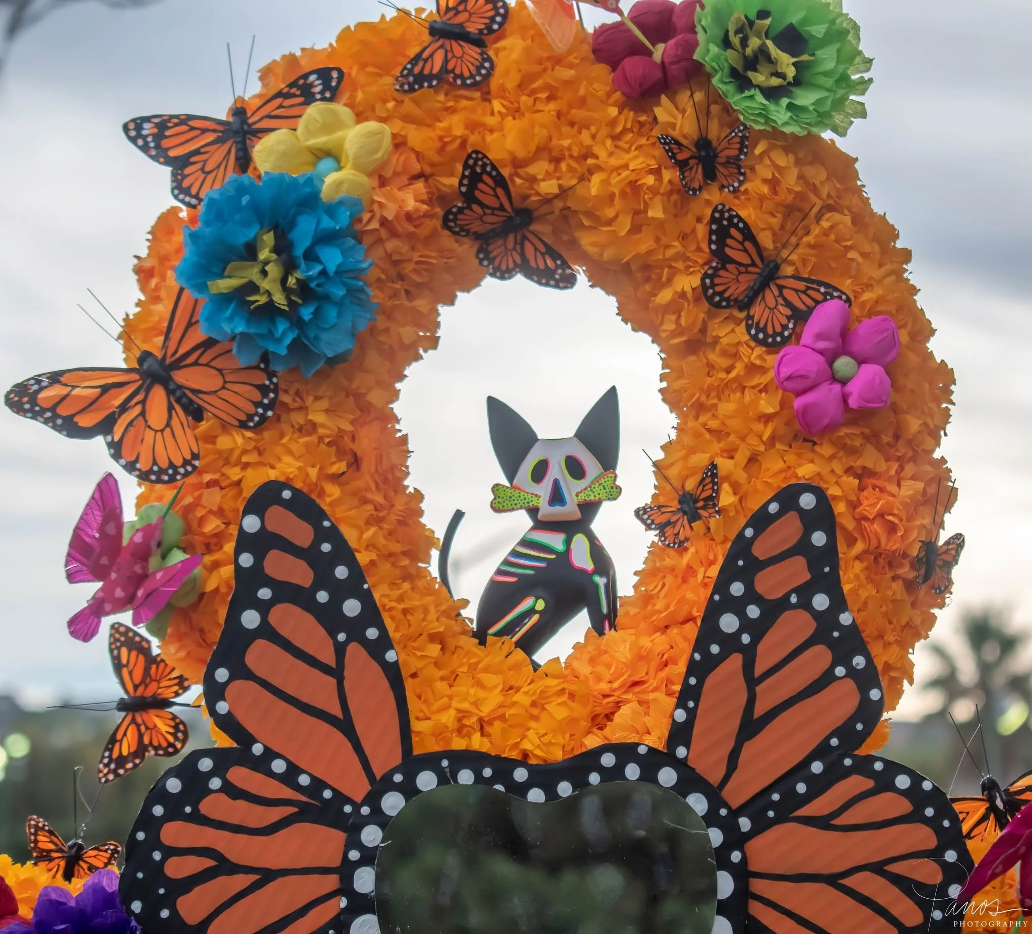Colorful Día de los Muertos altar decoration with orange flowers, monarch butterflies and a cat figure.