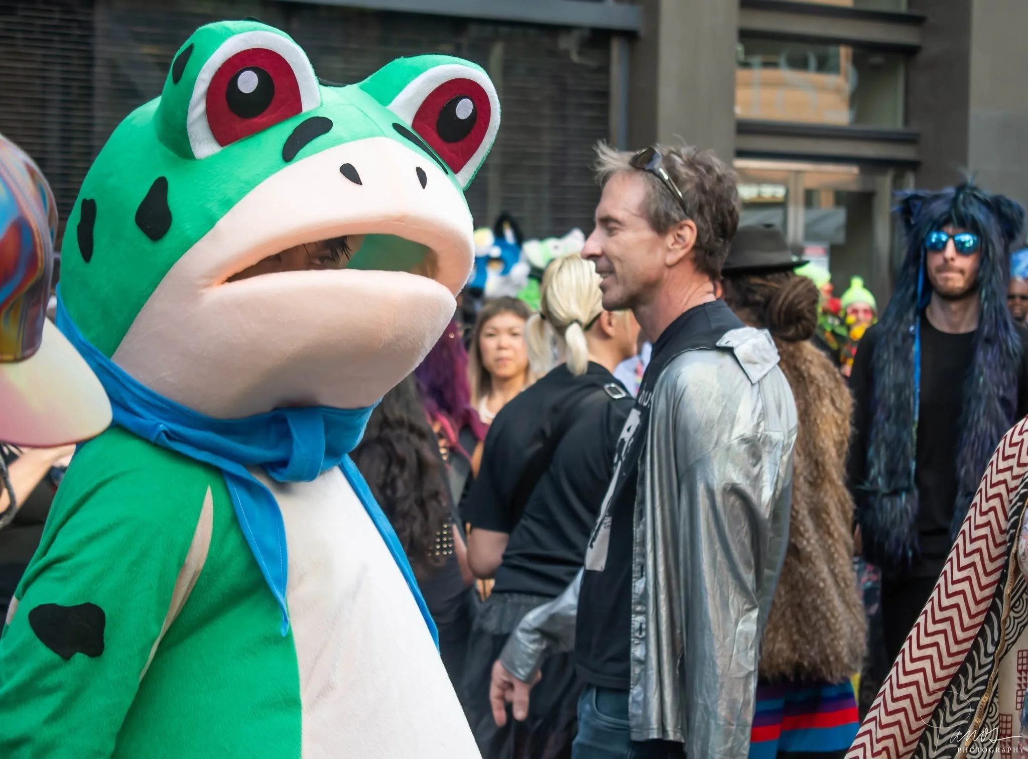 Festival participant in a large green frog costume among the crowd at the How Weird Street Faire in San Francisco.