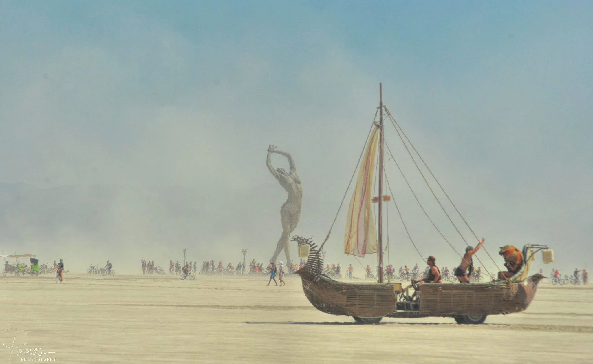 Boat-shaped Mutant Vehicle crosses the playa at Burning Man 2013, with a large art installation in the distance.