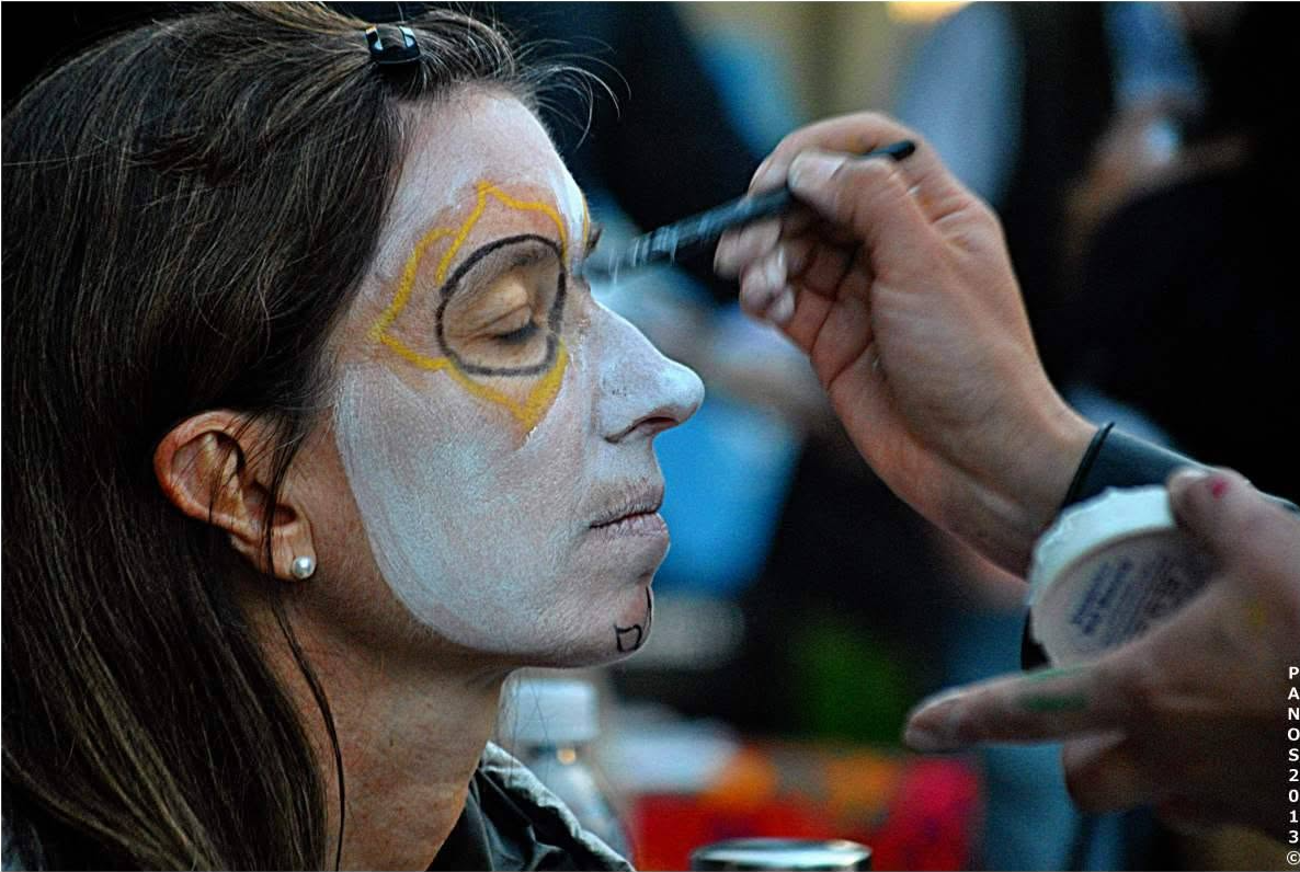 Woman having traditional Día de los Muertos face makeup applied during a San Francisco celebration.