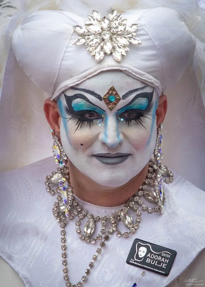Portrait of a Sister of Perpetual Indulgence wearing a white jeweled habit and blue theatrical makeup