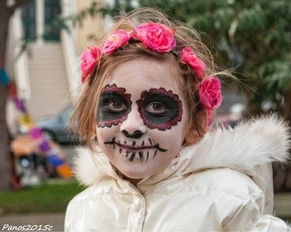 Child wearing Día de los Muertos face paint and a crown of pink flowers during a San Francisco celebration.