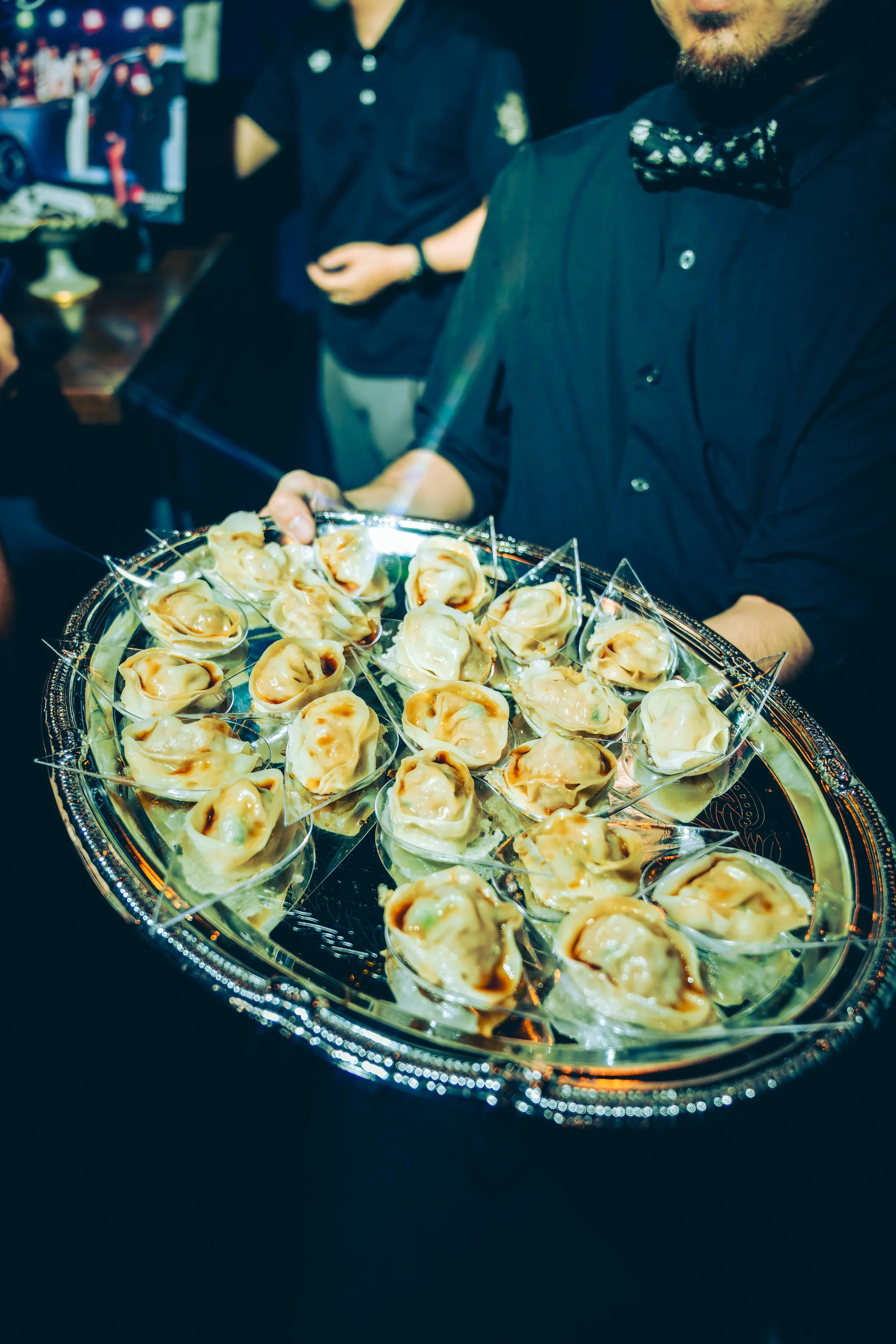 A waiter serving a tray of small, sliced dumplings with sauce at a social event or restaurant.