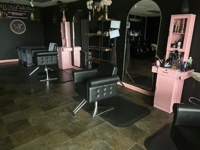 Inside a modern hair salon with black and pink furniture, including styling chairs, shelves with hair products, and professional equipment.