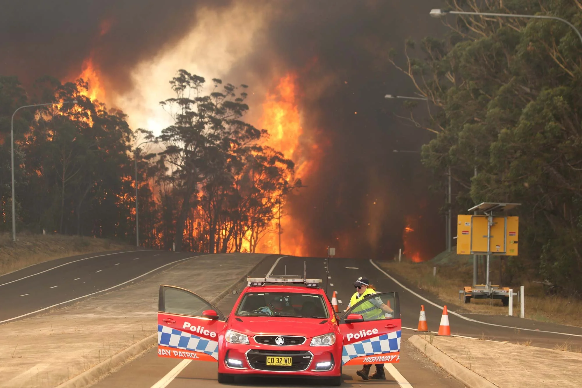  Flames burst out of the state forest crowning through the top of the trees and cross the princes highway at the Sussex inlet intersection south of Nowra this afternoon.   Tuesday 31st December 2019. Guardian Australia. 