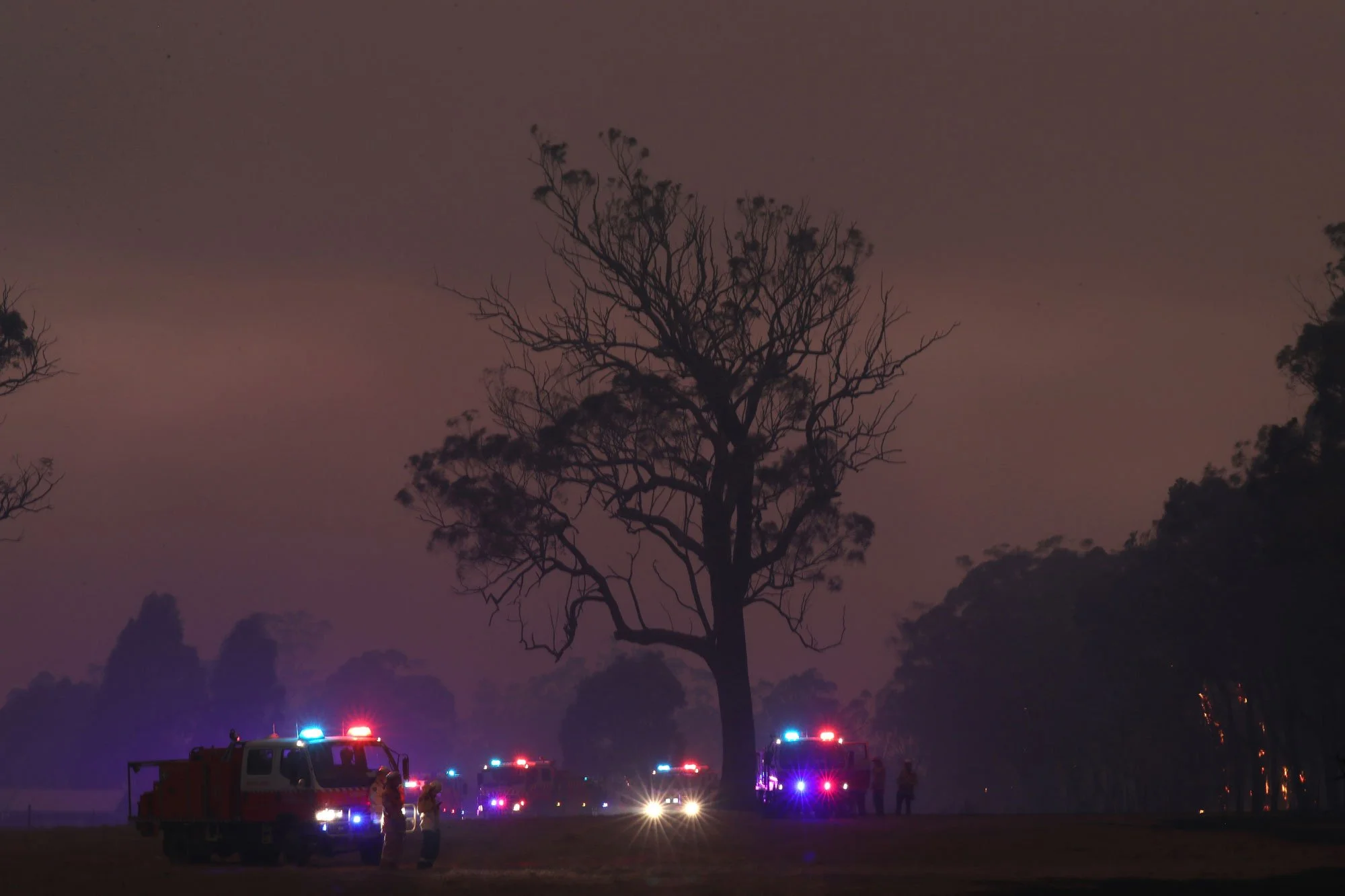  RFS crews fight a fire at the Green Wattle Creek fire near Bargo NSW tonight as it starts to rain.   21st December 2019. Guardian Australia. 