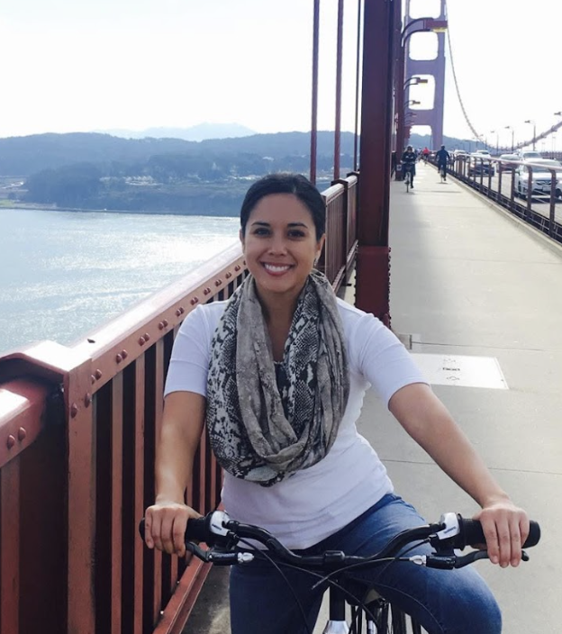 A woman smiling while sitting on a bicycle on the Golden Gate Bridge in San Francisco, California.