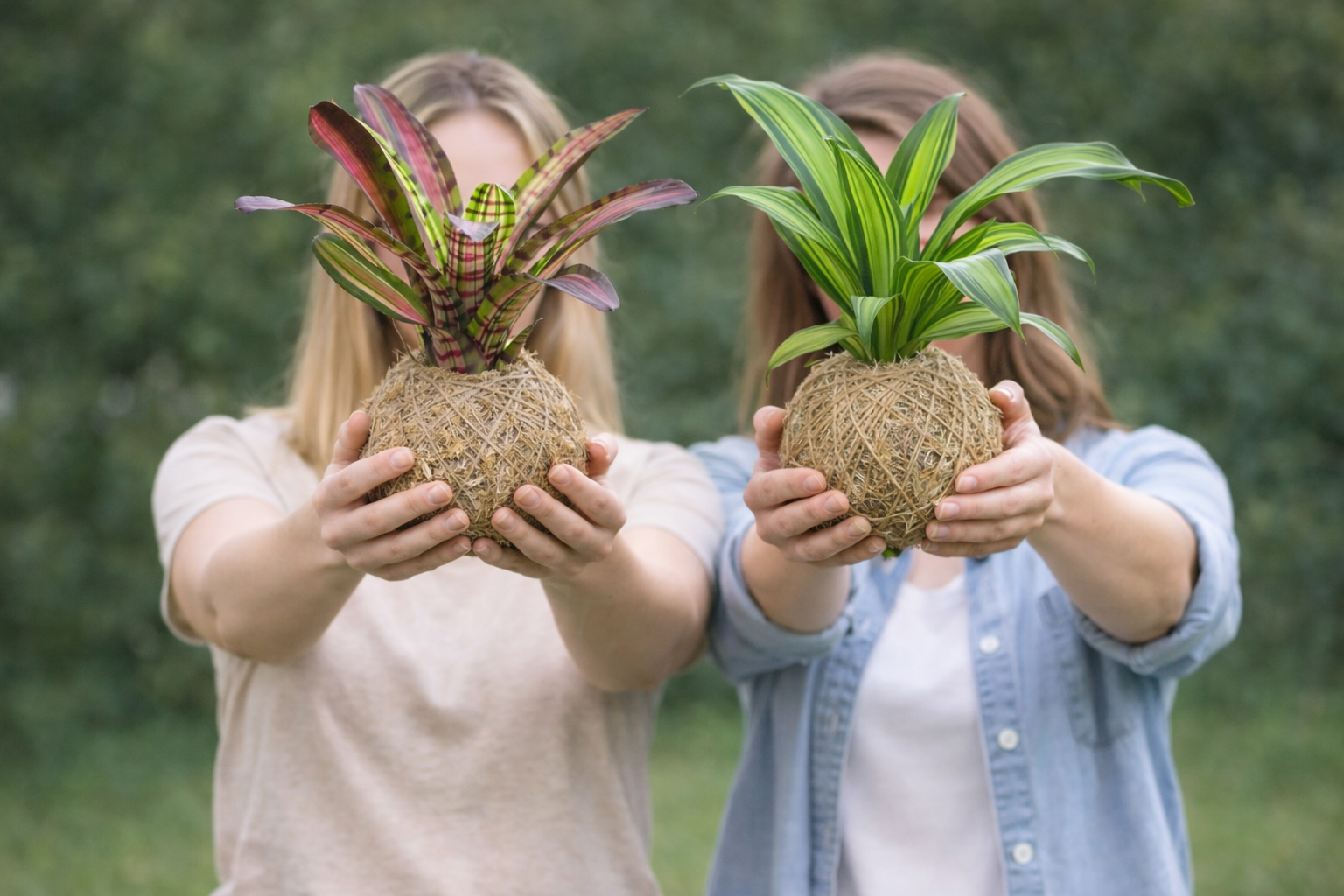 Two people holding handcrafted kokedama moss ball plants in front of them, faces gently hidden, symbolizing a shared and intimate plant-making experience.