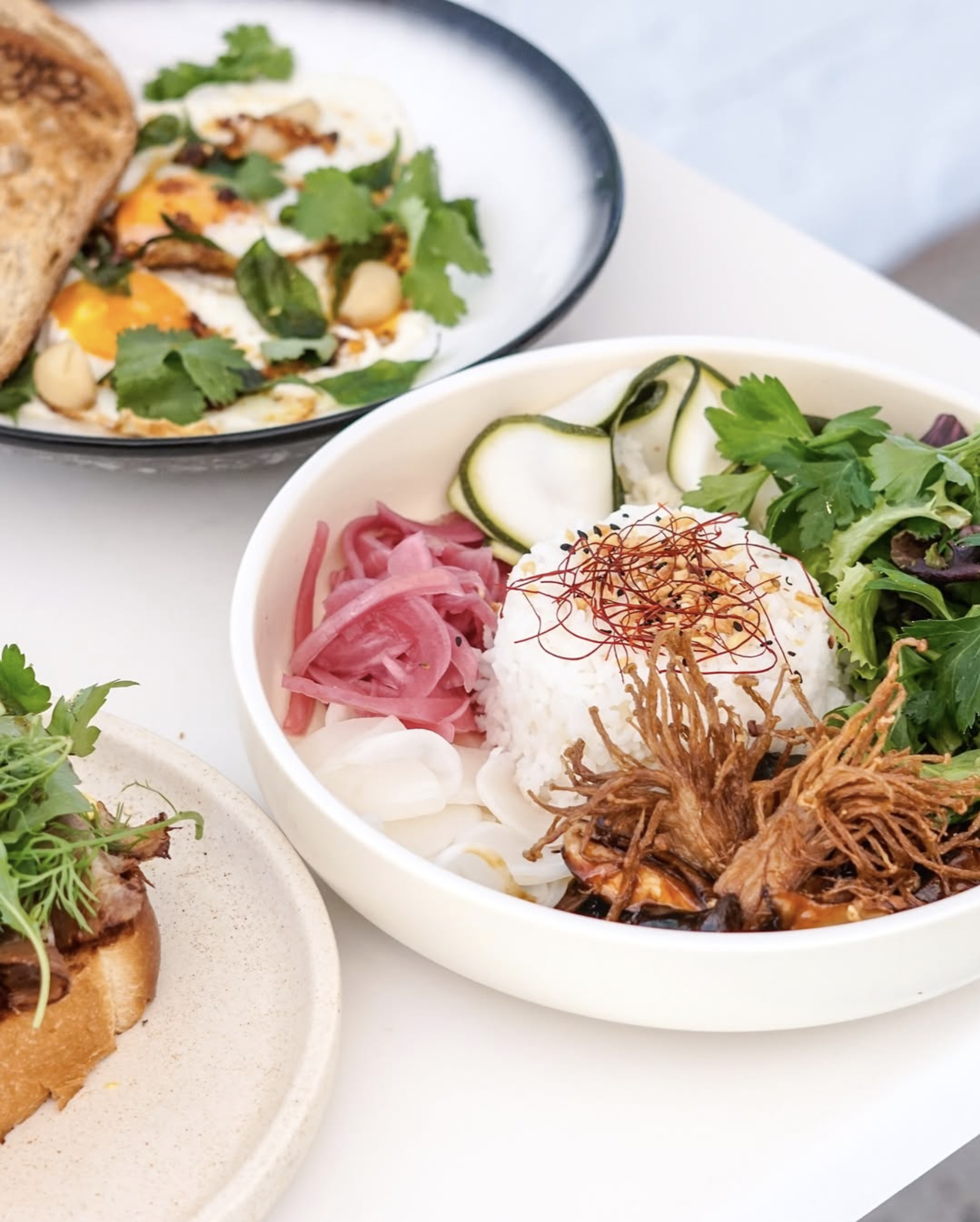 A bowl of Korean bibimbap with rice, shredded meat, pickled vegetables, fresh greens, and sliced cucumbers, with various garnishes.