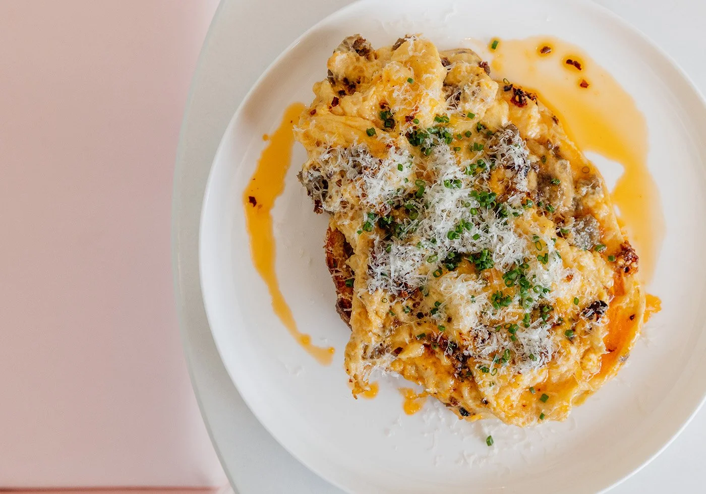Oven-baked French toast topped with grated cheese, chopped chives, and herbs, drizzled with syrup, on a white plate.