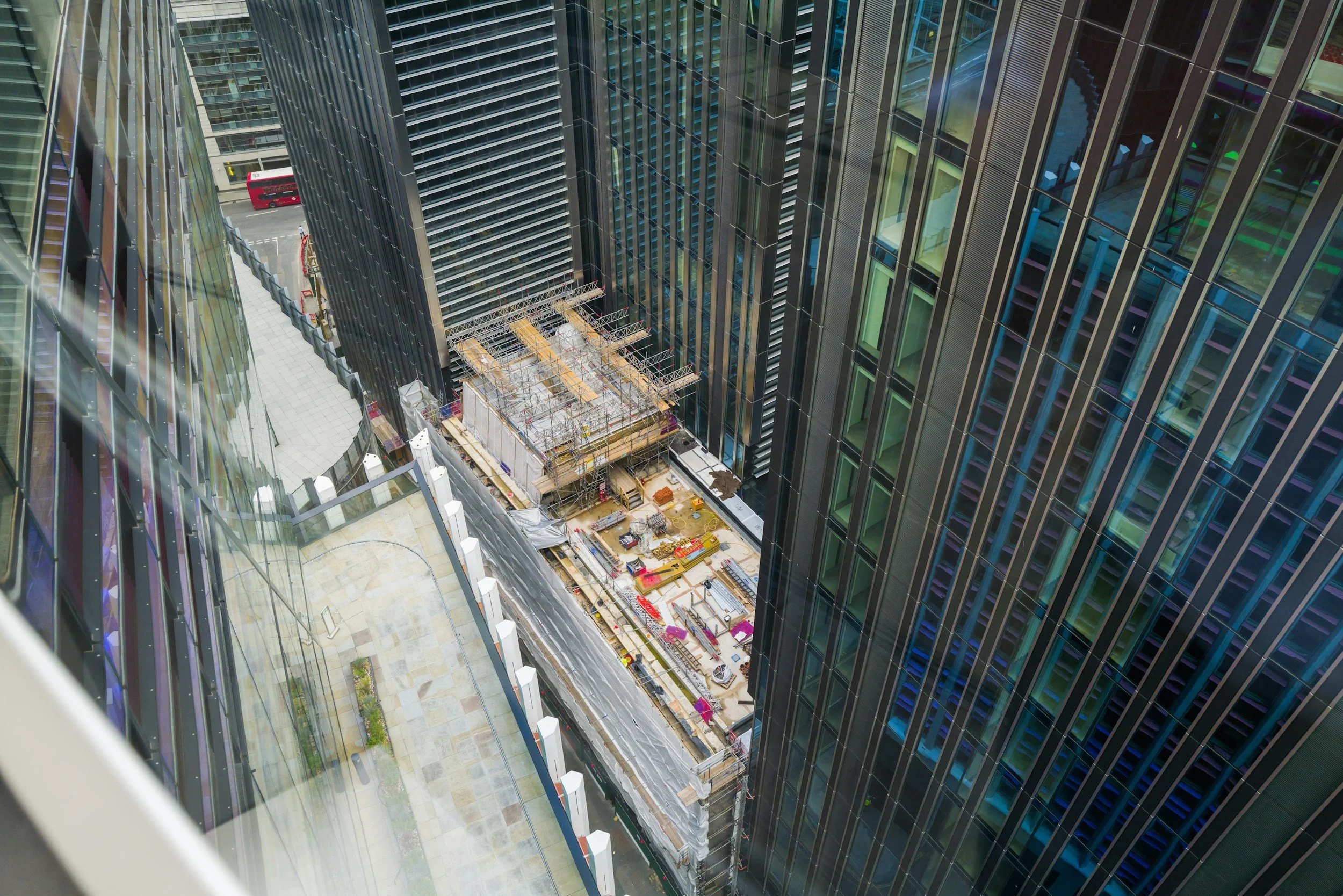View from above of a construction site inside a high-rise city building, with scaffolding and building materials, surrounded by glass skyscrapers.