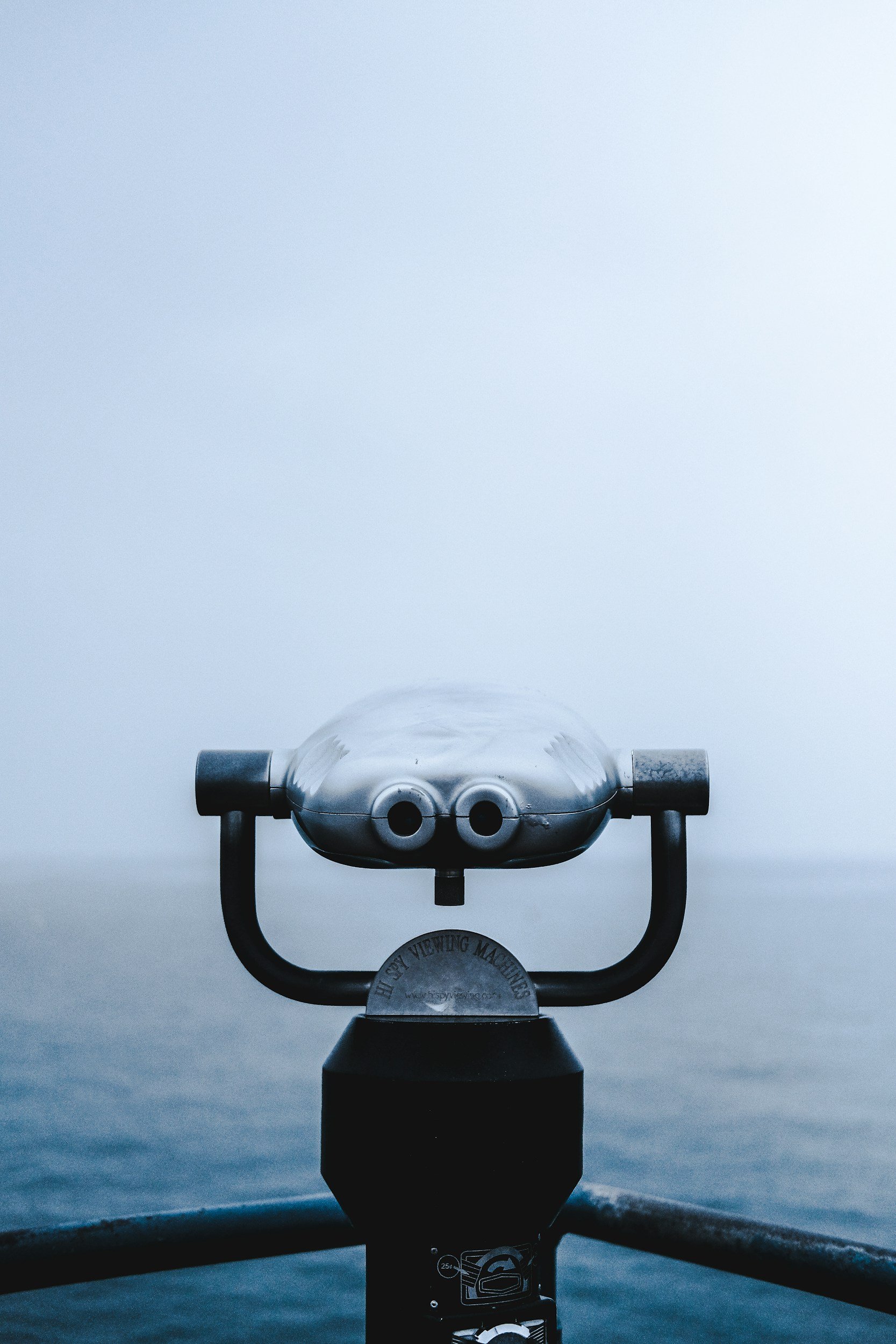 Image of a steel binocular overlooking a foggy ocean view.