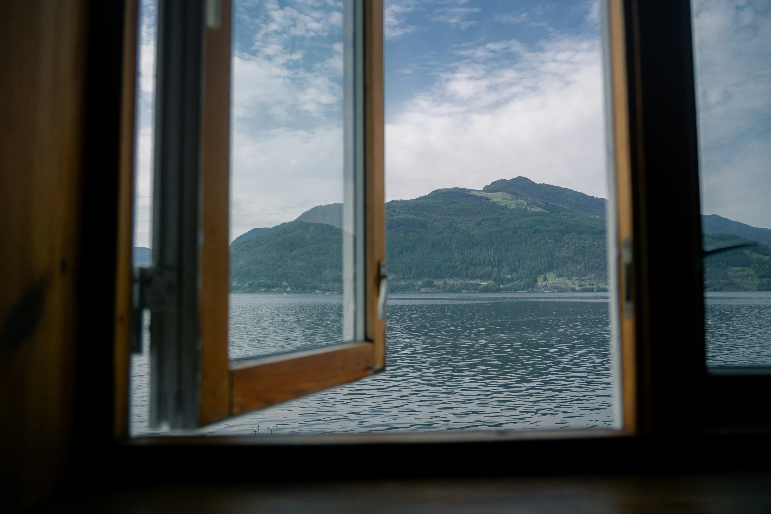 View of a lake with mountains in the distance through an open window.