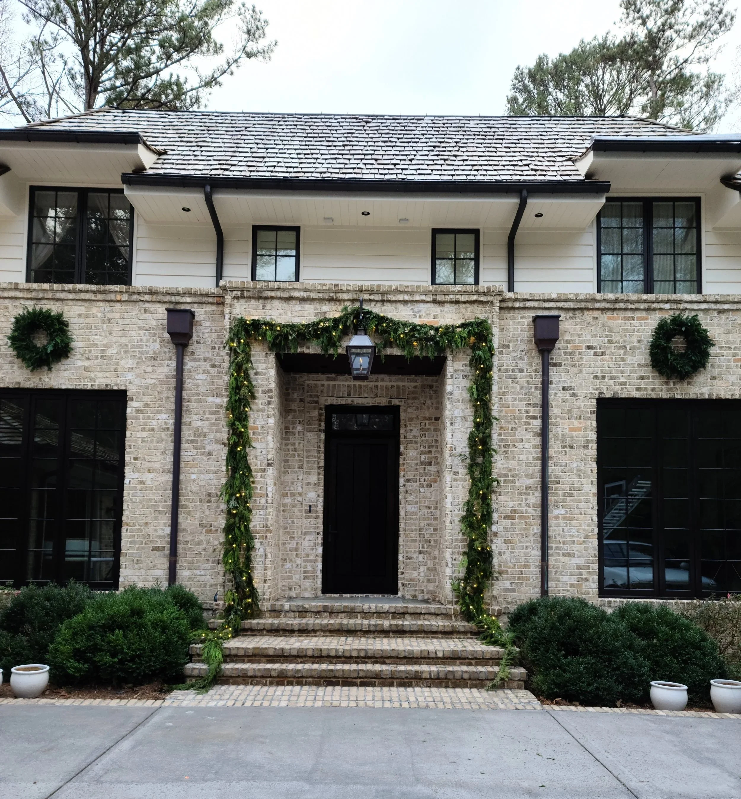 Exterior view of a two-story house decorated for the holidays with green garland and wreaths, black front door, brick stairs, and potted plants. Light Up Atlanta
