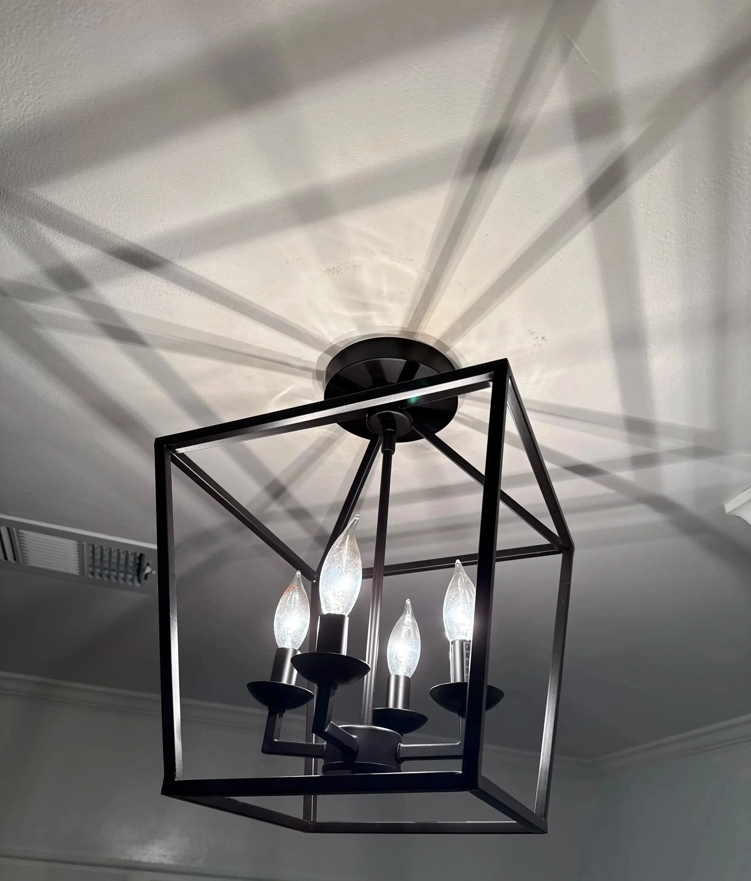 Modern black geometric chandelier with five candle-shaped light bulbs hanging from a ceiling Light Up Atlanta