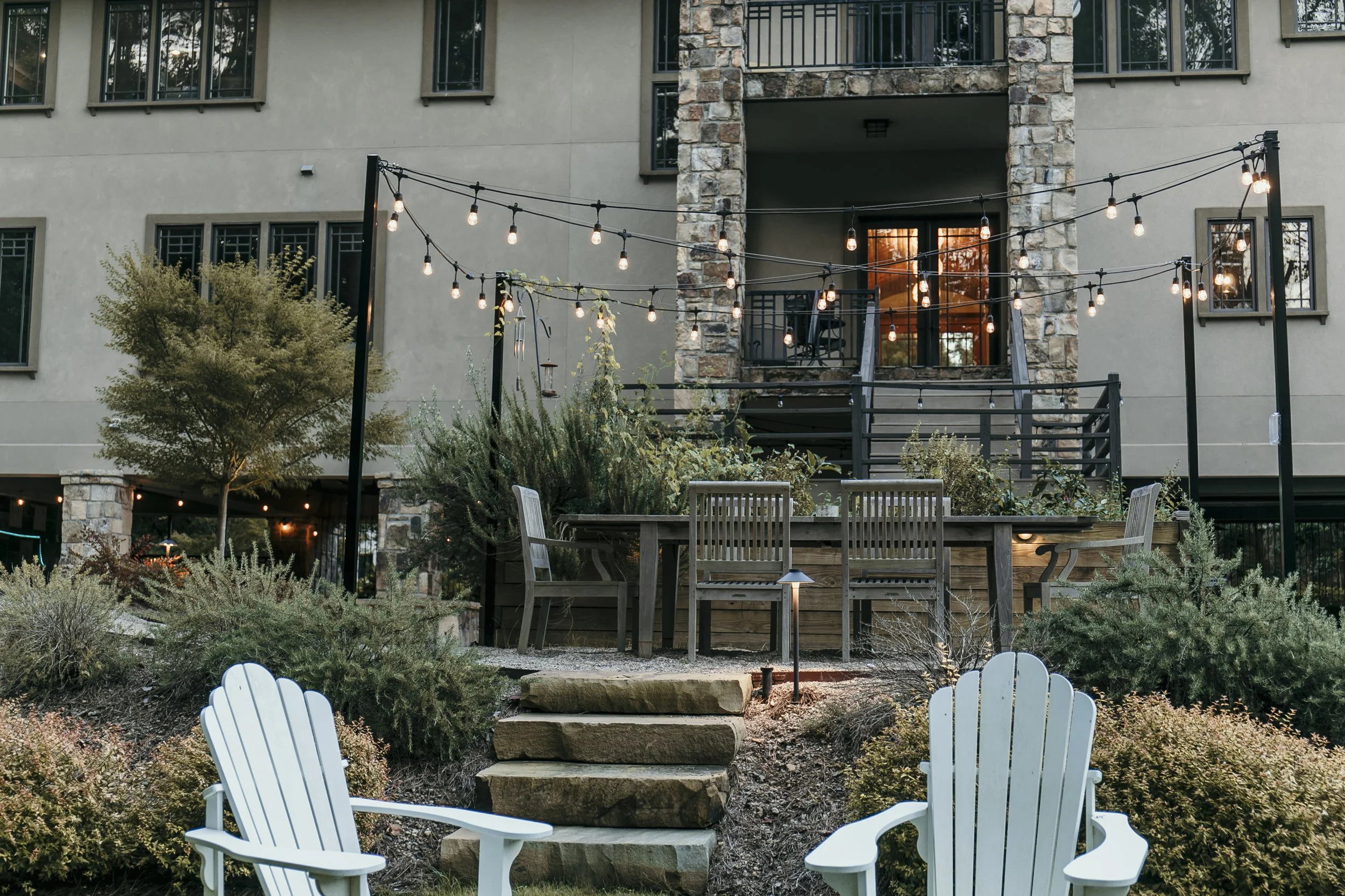 Outdoor patio area with string lights, wooden chairs, and garden plants in front of a multi-story residential building. Light Up Atlanta