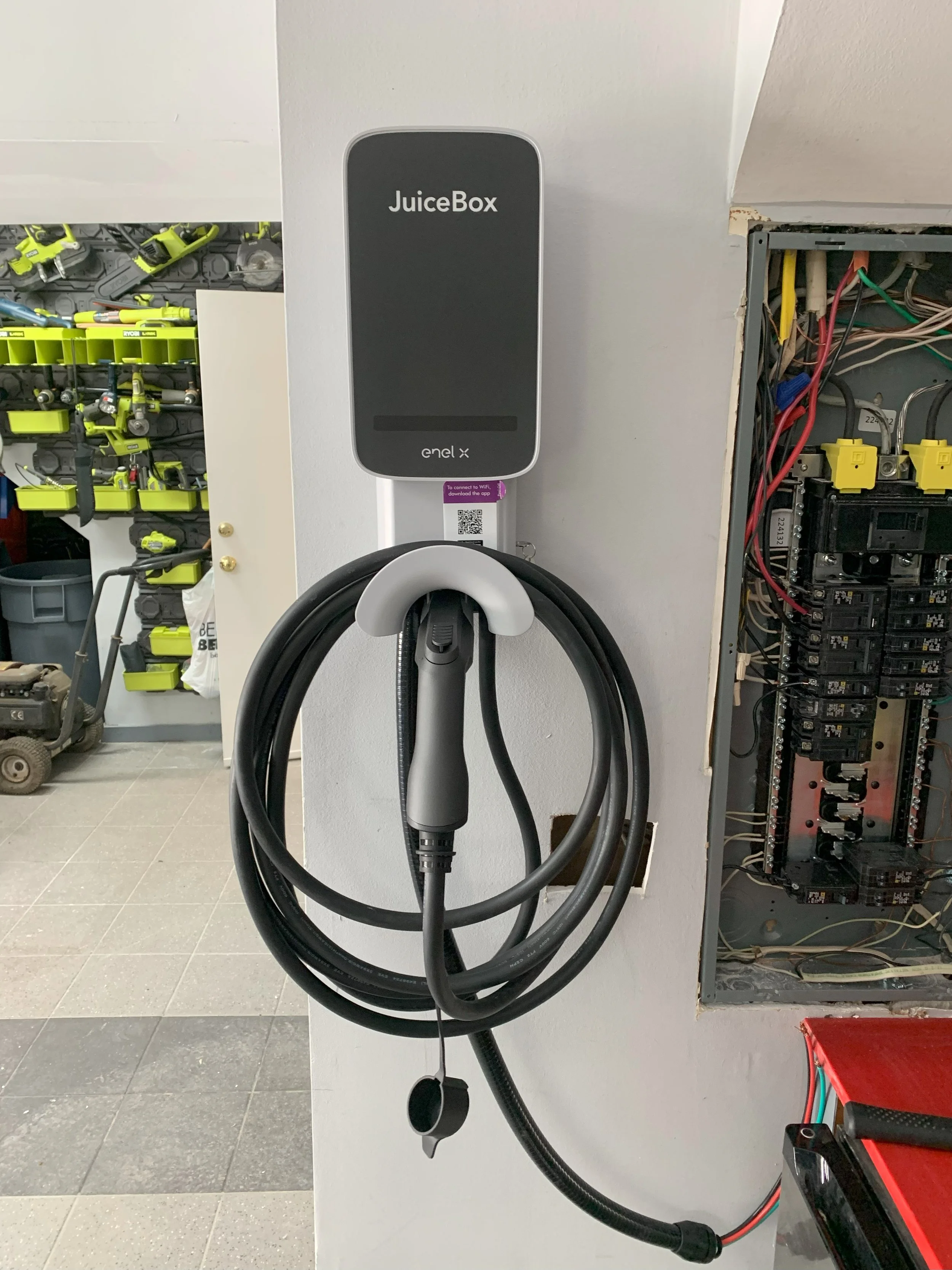 An electric vehicle charging station with a charging cable hanging on a wall, labeled JuiceBox by Enel X, in a workshop or maintenance area. Light Up Atlanta