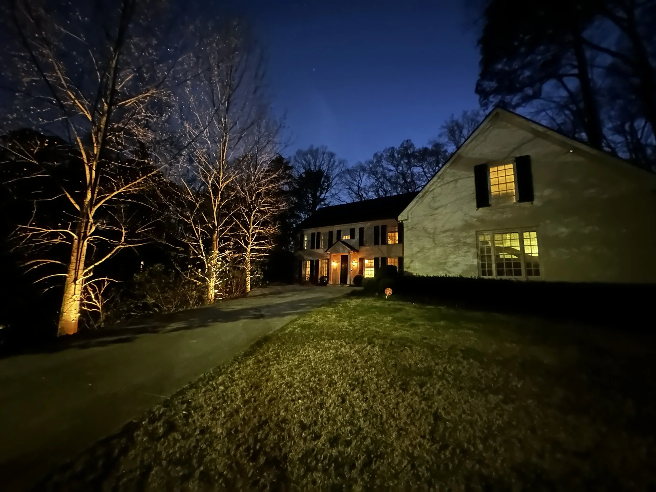 A house with lit windows at night, surrounded by trees and a maintained lawn. Light Up Atlanta