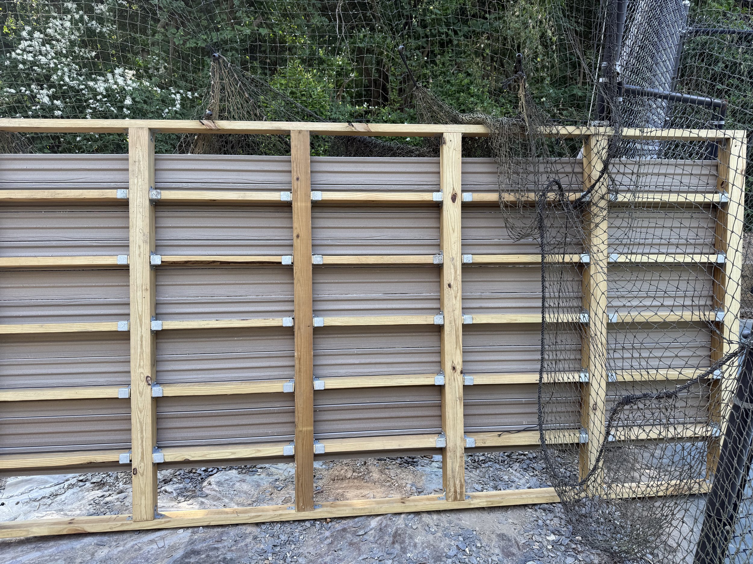 Wooden and metal fence structure with black netting, outdoors with greenery in the background. Light Up Atlanta