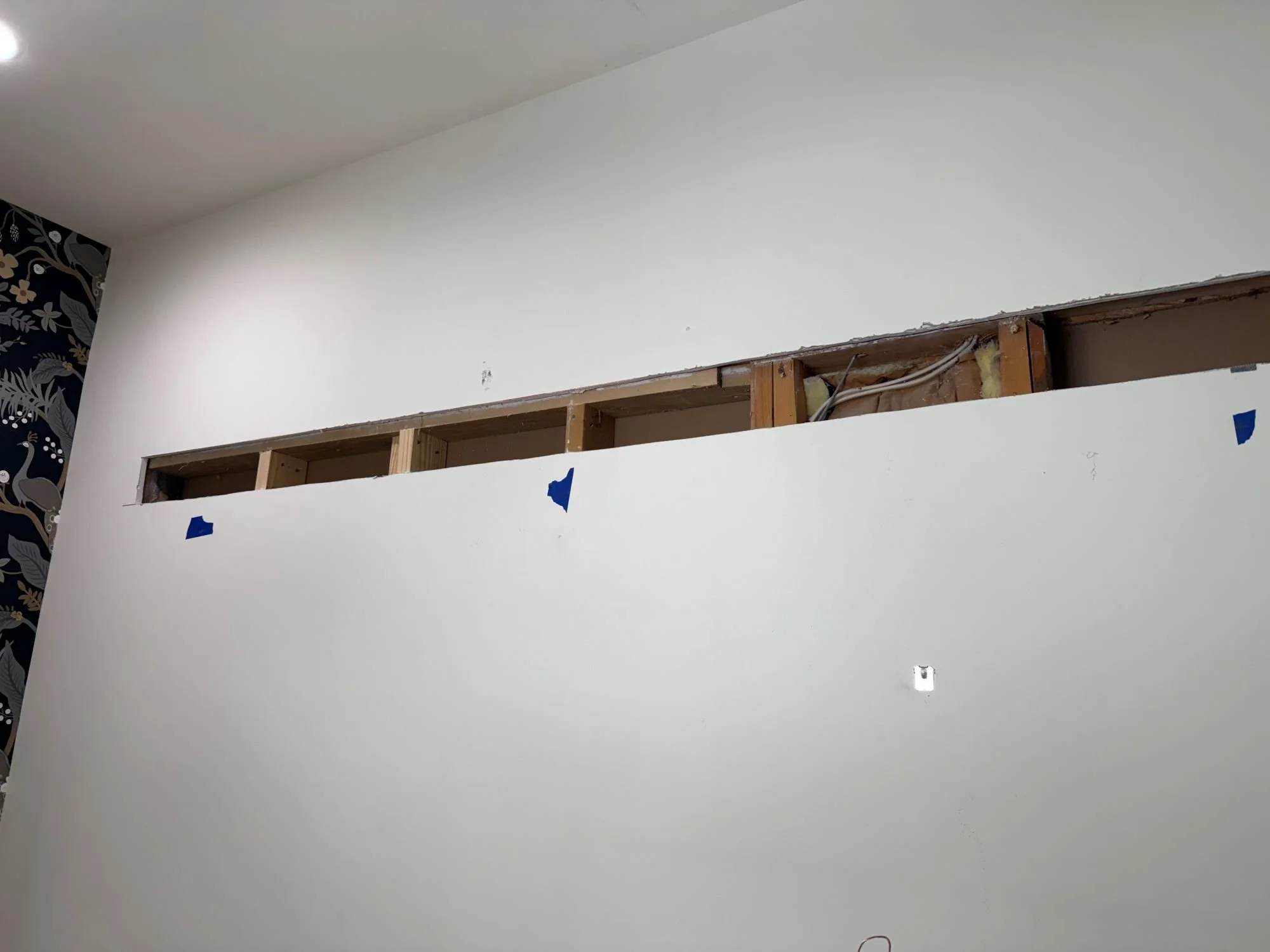 Interior wall under construction with exposed wooden studs and a partially installed drywall panel. Light Up Atlanta