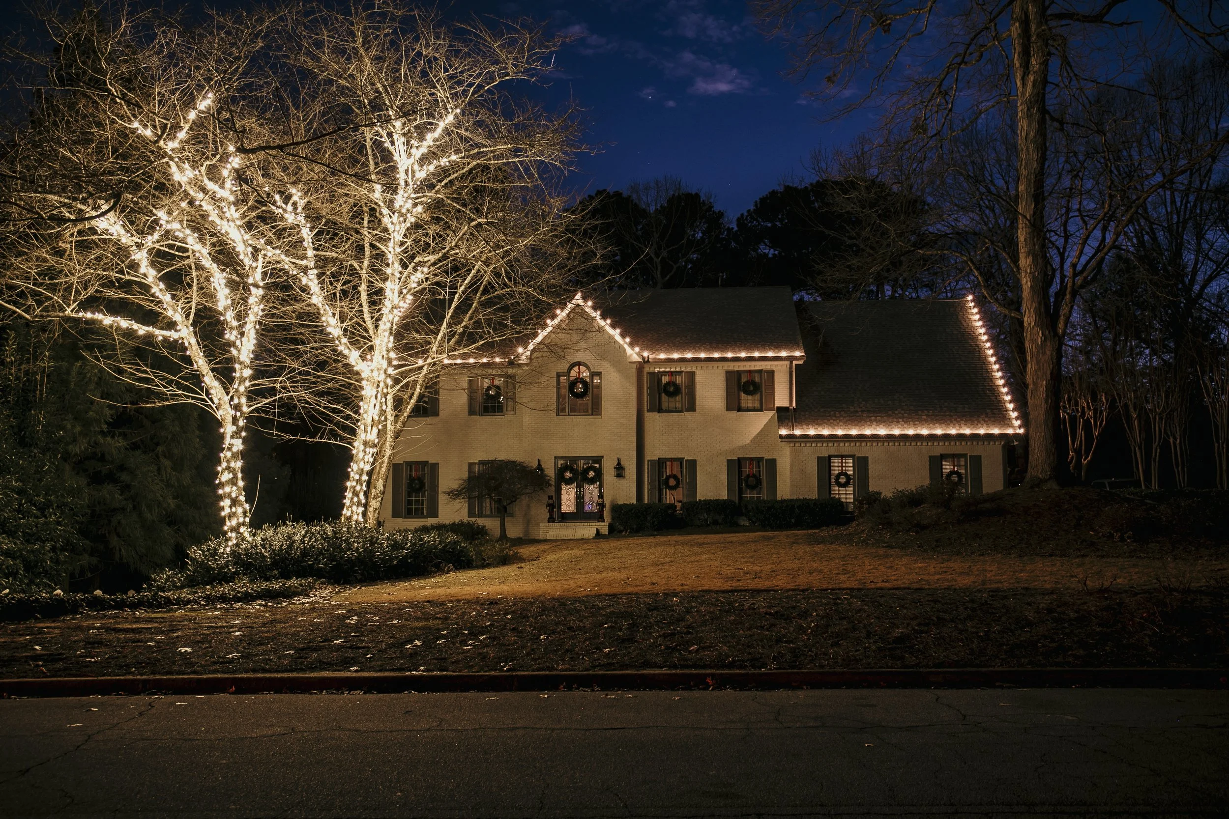 A two-story house decorated with Christmas lights and wreaths at night.