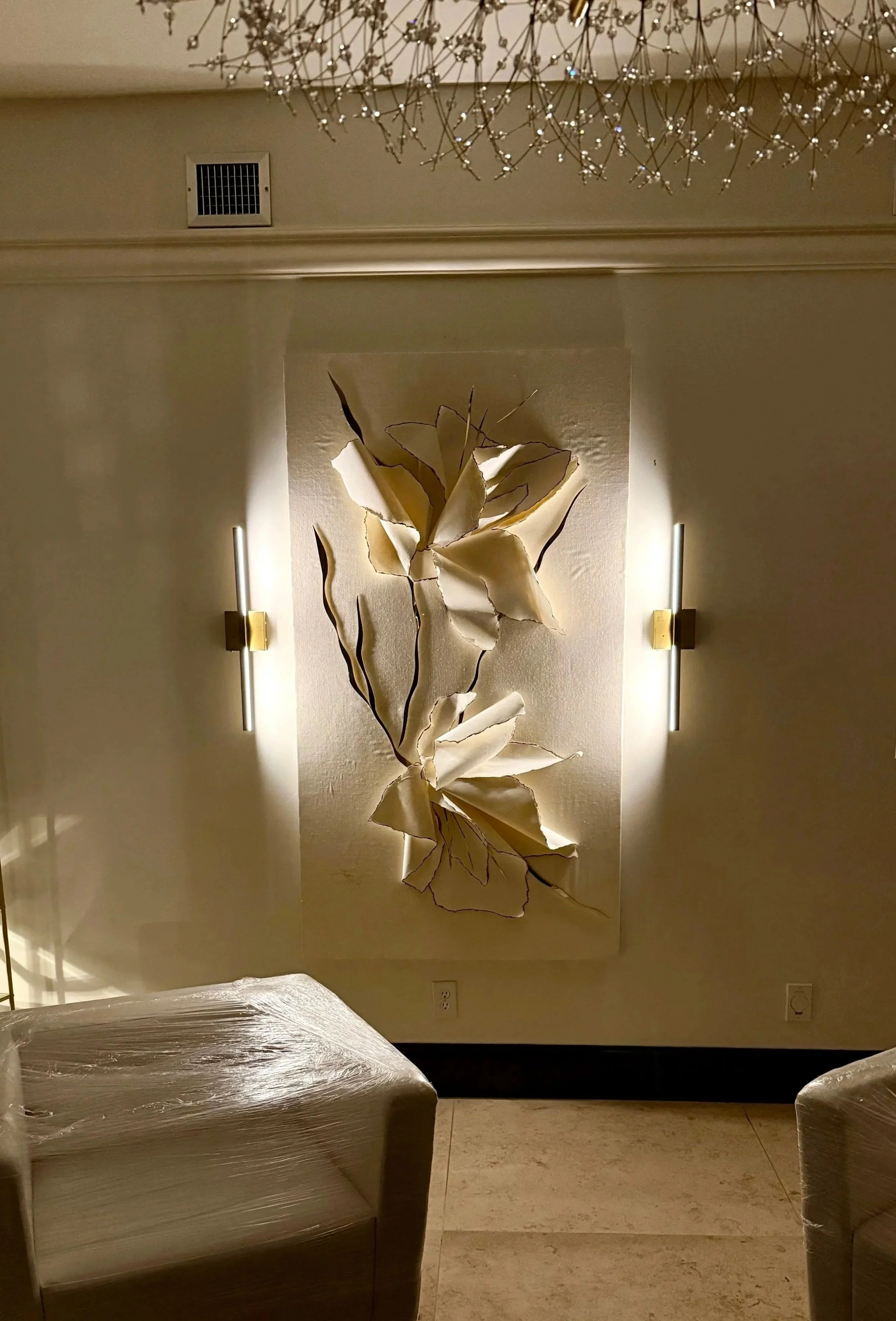 Decorative wall art with illuminated metal flowers and branches, flanked by vertical wall sconces, with lounge chairs covered in plastic in the foreground. Light Up Atlanta