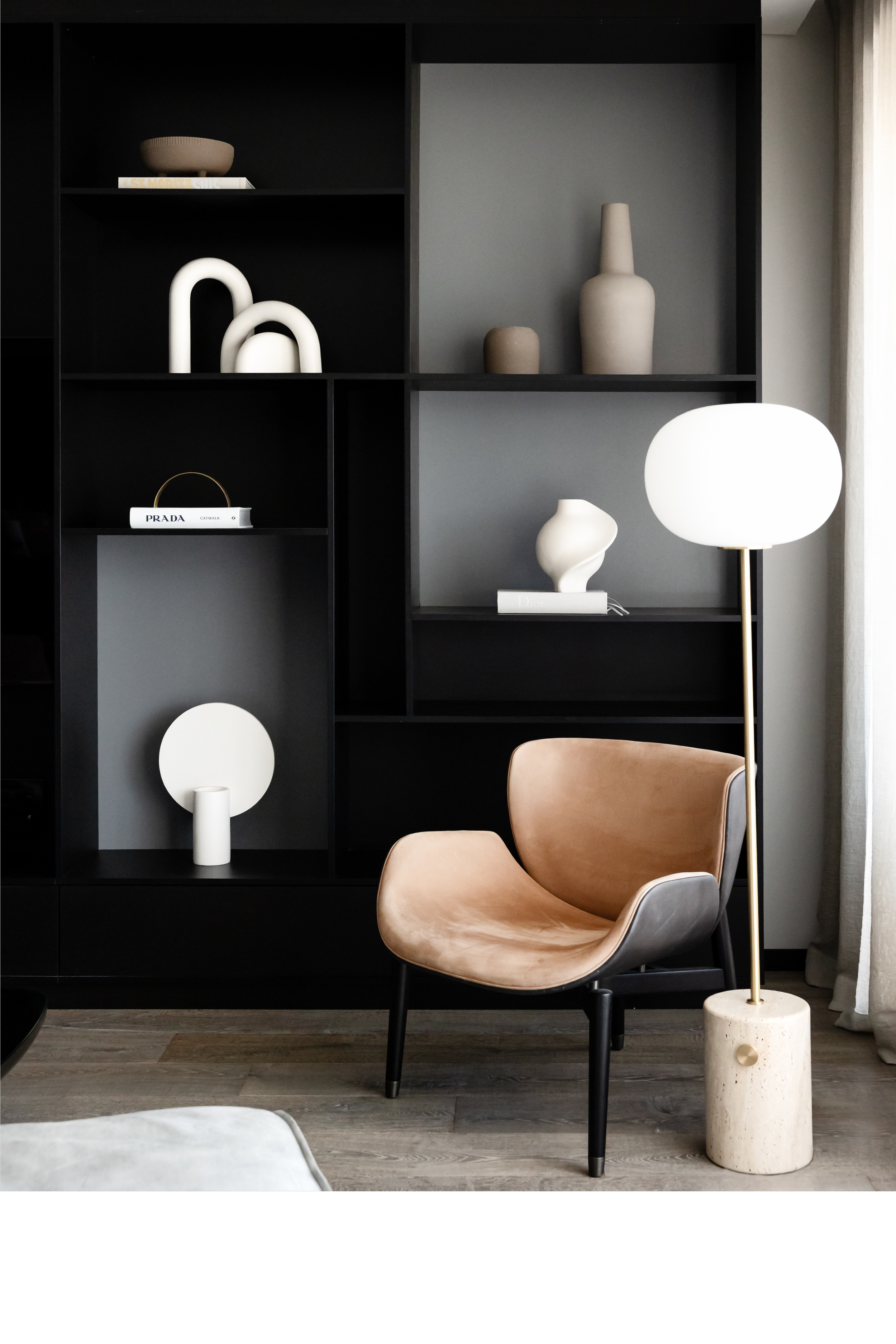 Contemporary living room featuring black built-in shelving, sculptural objects, and a modern leather lounge chair in a refined interior.