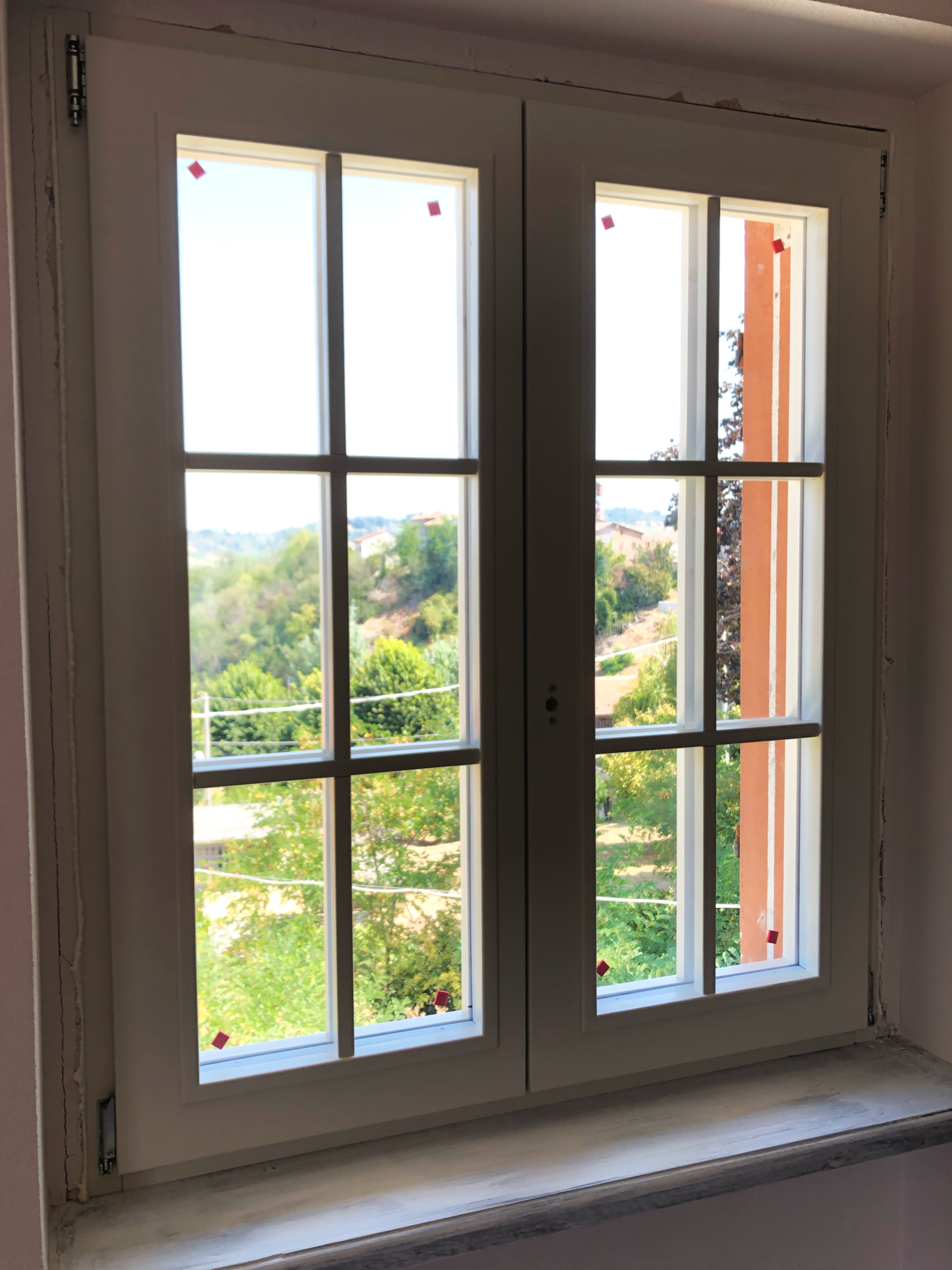 Finestra a doppio battente con vetri suddivisi in sei pannelli, vista panoramica su un paesaggio verde e colline.