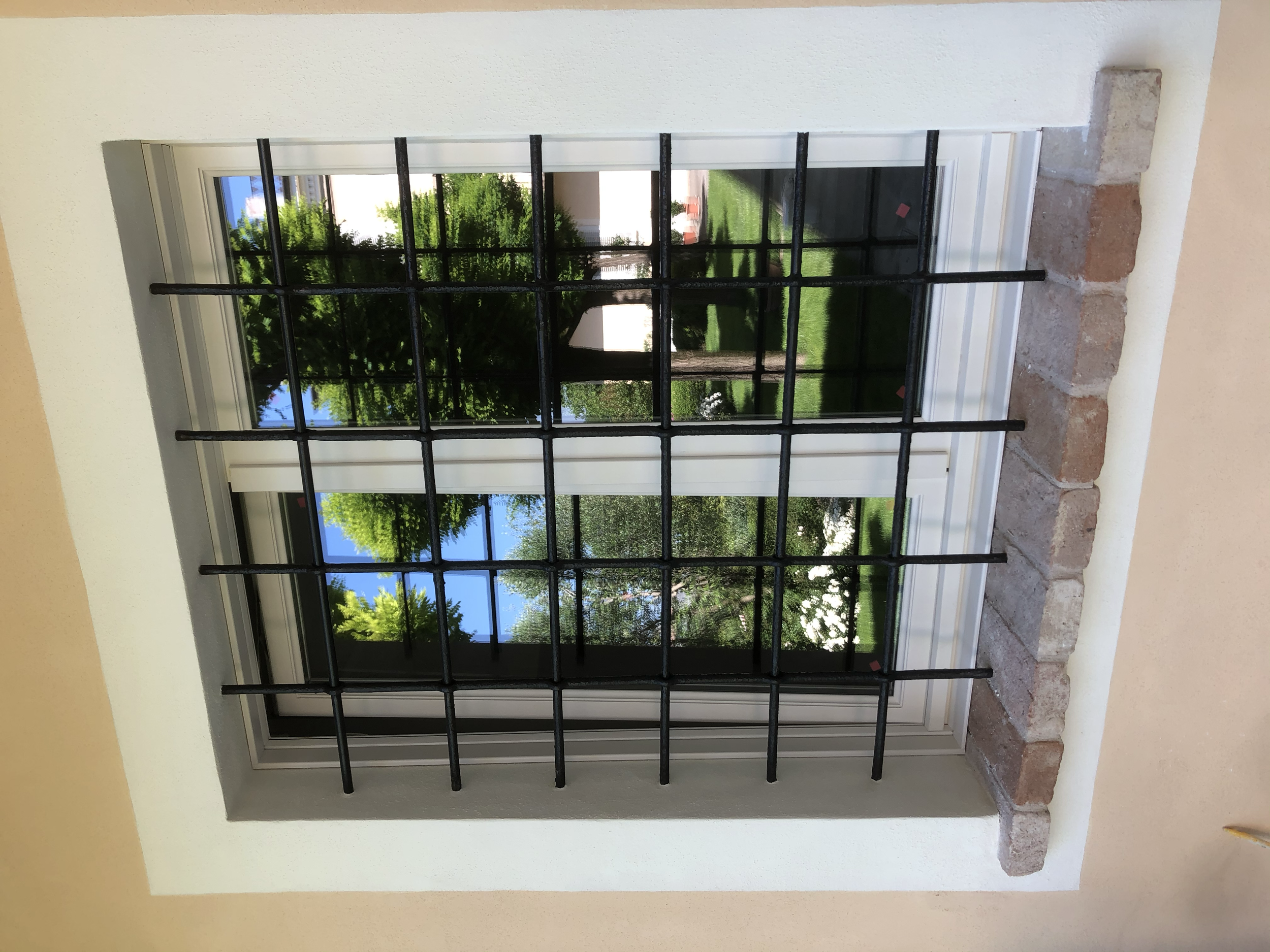 Finestra con grate nere, vista di alberi e prato verde all'esterno.