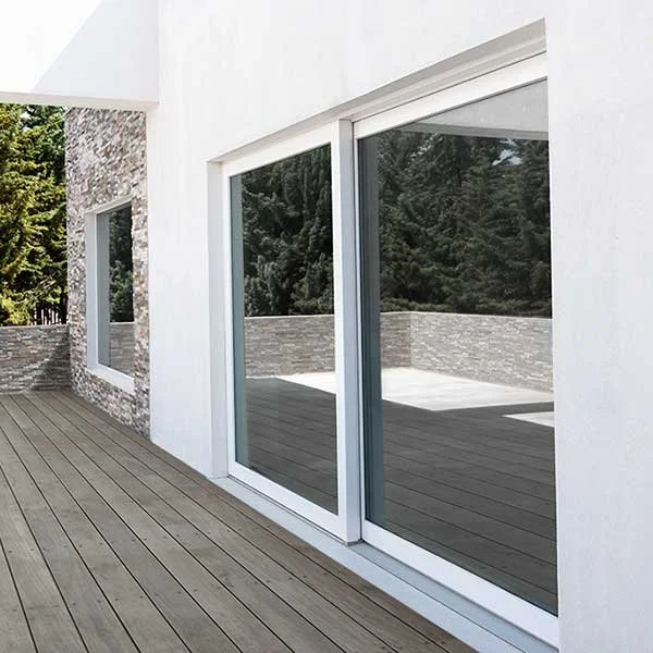 Vista di una terrazza di un edificio moderno con grandi finestre in vetro e pareti biachi, con sfondo alberi verdi.