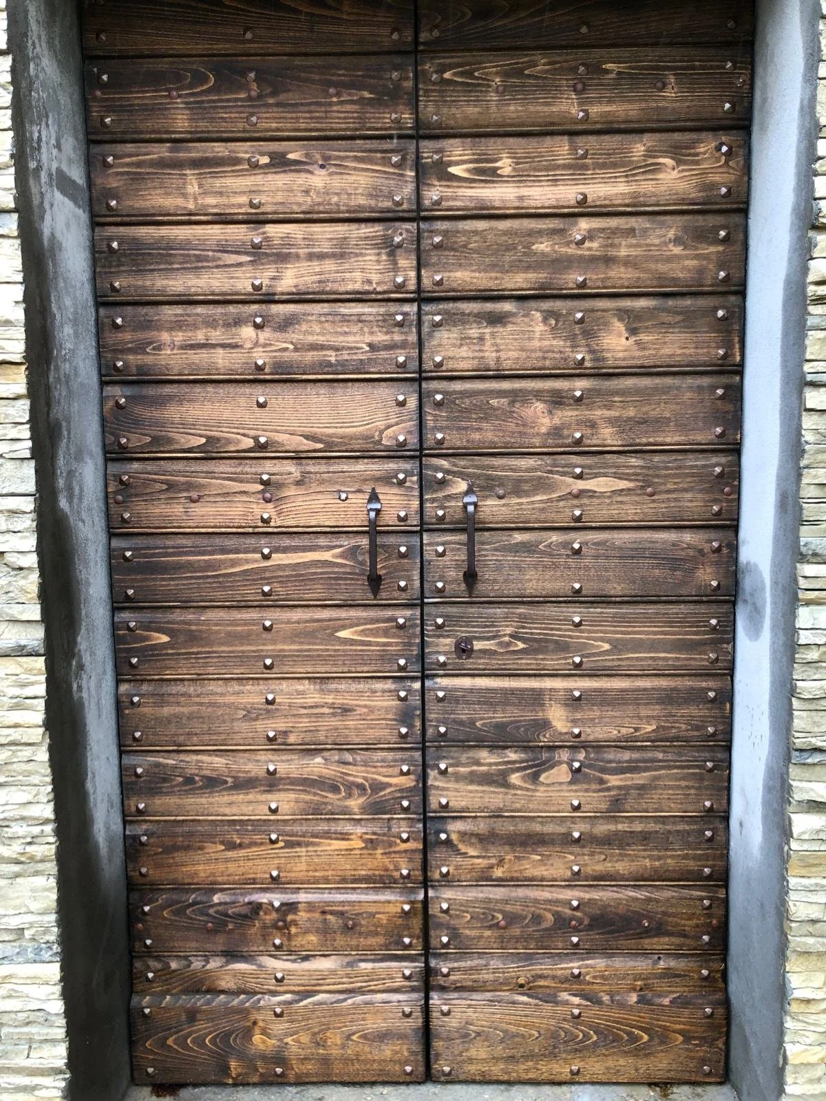 Porta in legno con maniglie nere e grandi rivetti in ferro, circondata da muri in pietra.
