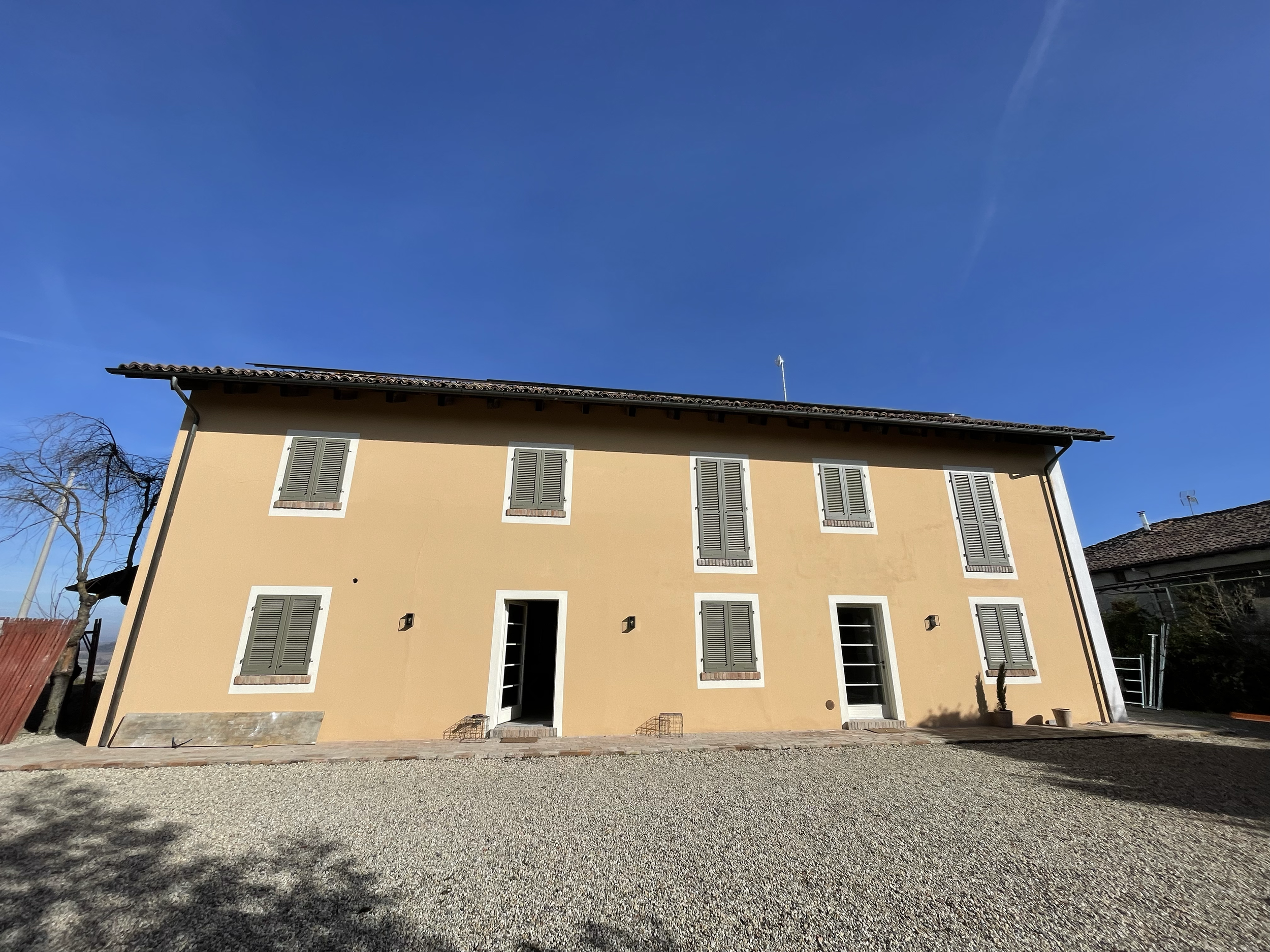 Edificio residenziale con pareti gialle, finestre con persiane grigie, porta centrale e giardino di ghiaia davanti.