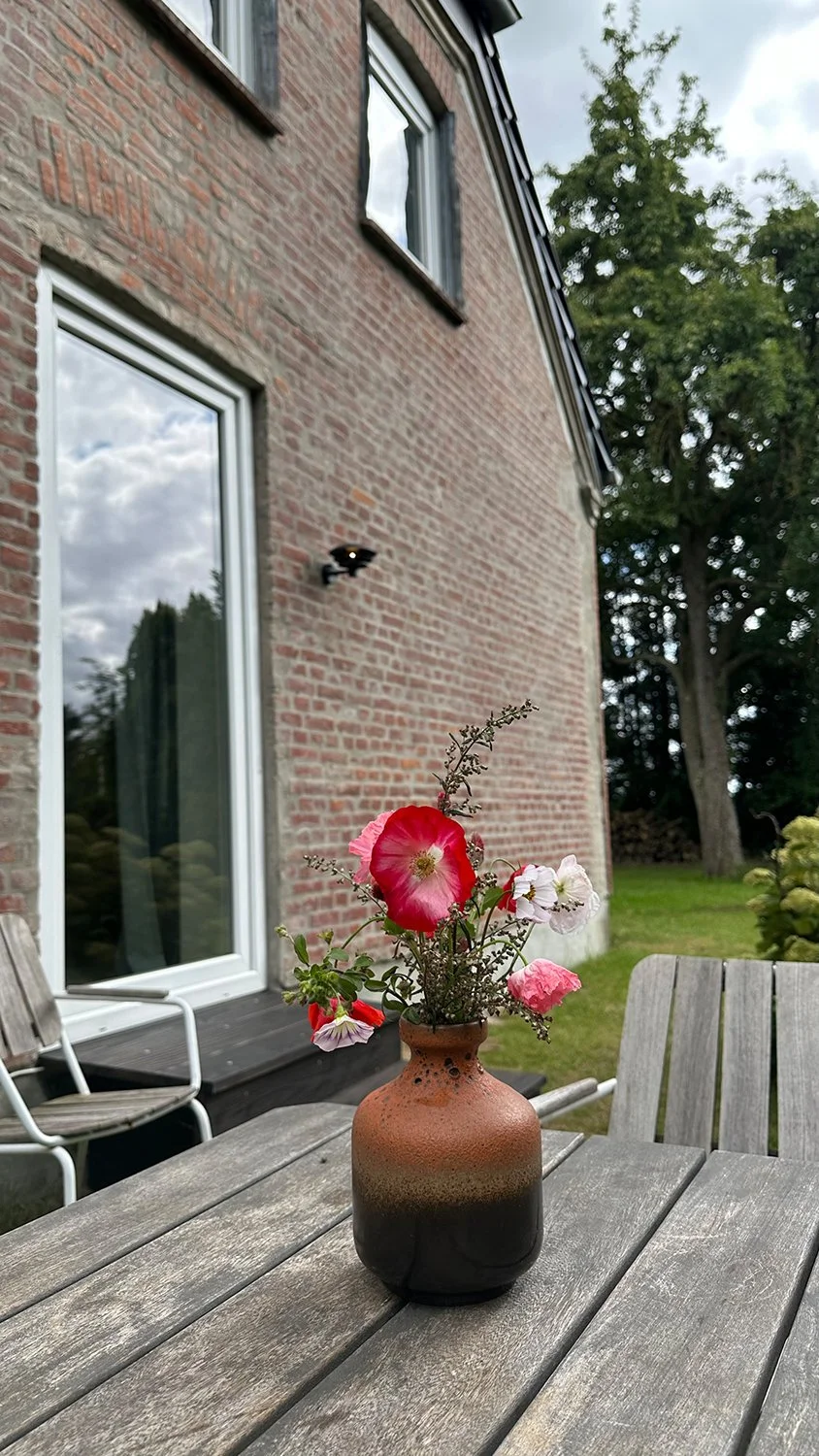 Terrasse des Ferienhauses mit Tisch und Stühlen sowie Blumenstrauß