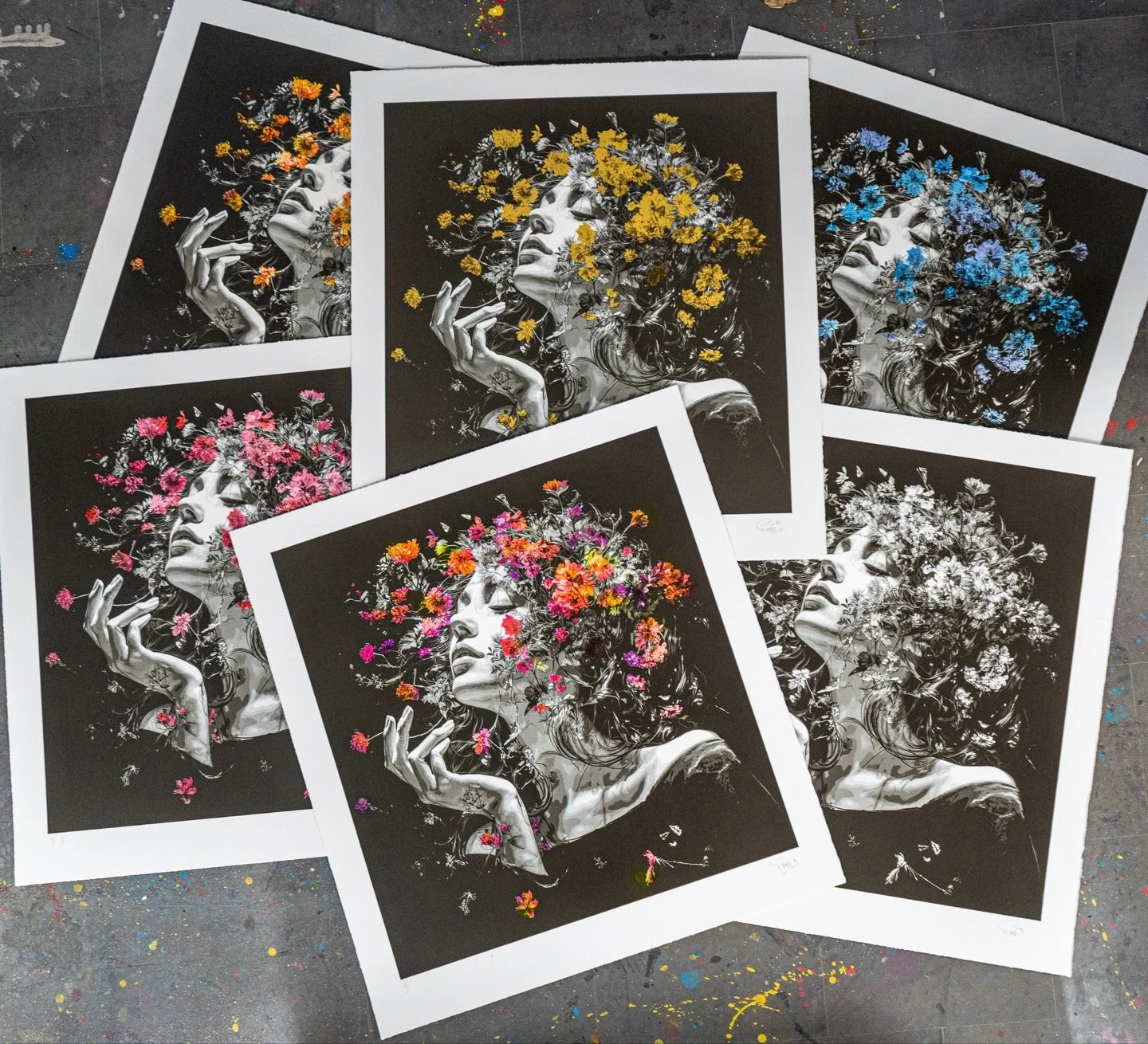 Several art prints of a woman with flowers in her hair, shown in black and white with colorful flowers overlayed in different colors, including yellow, pink, blue, and orange, laid on a speckled artist's table.
