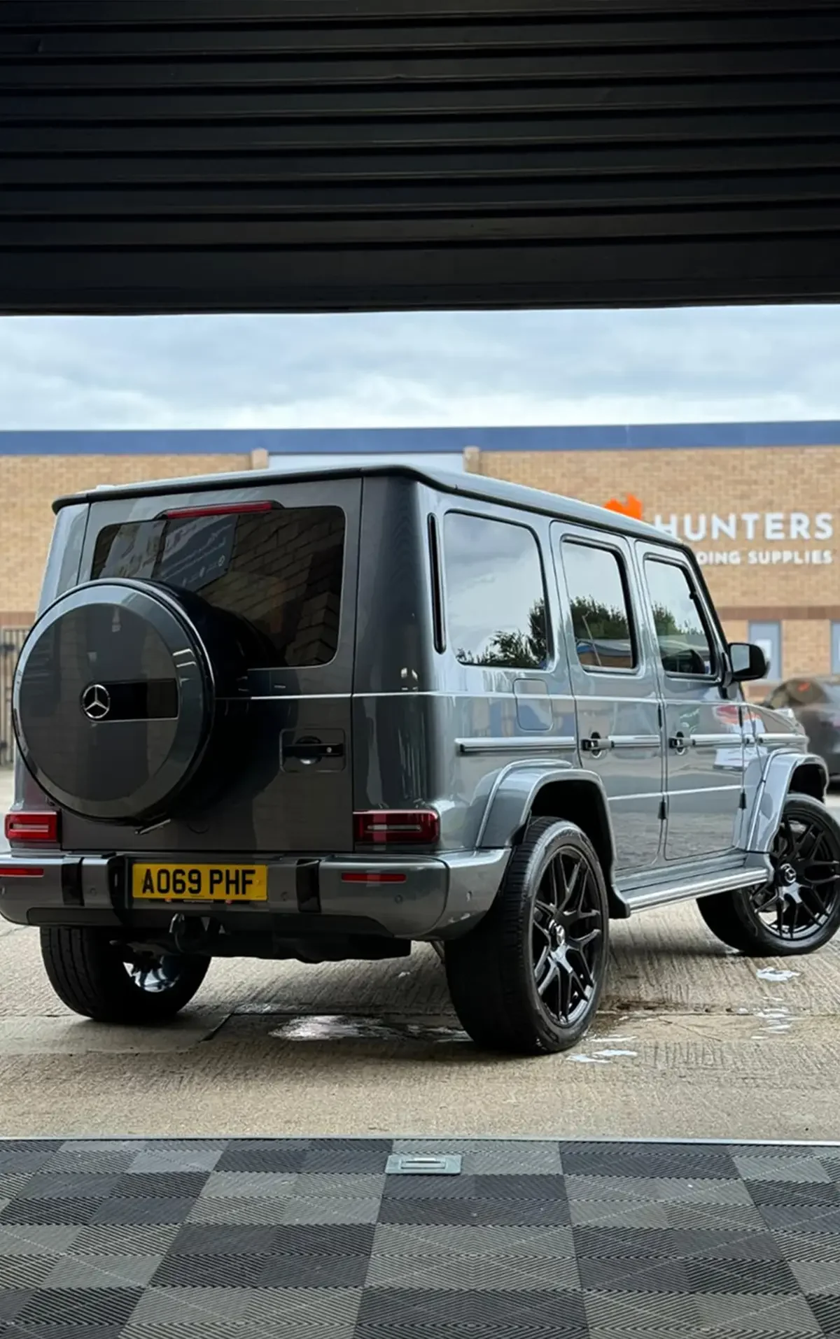 A silver Mercedes G-Class SUV is parked on a mat in front of a building