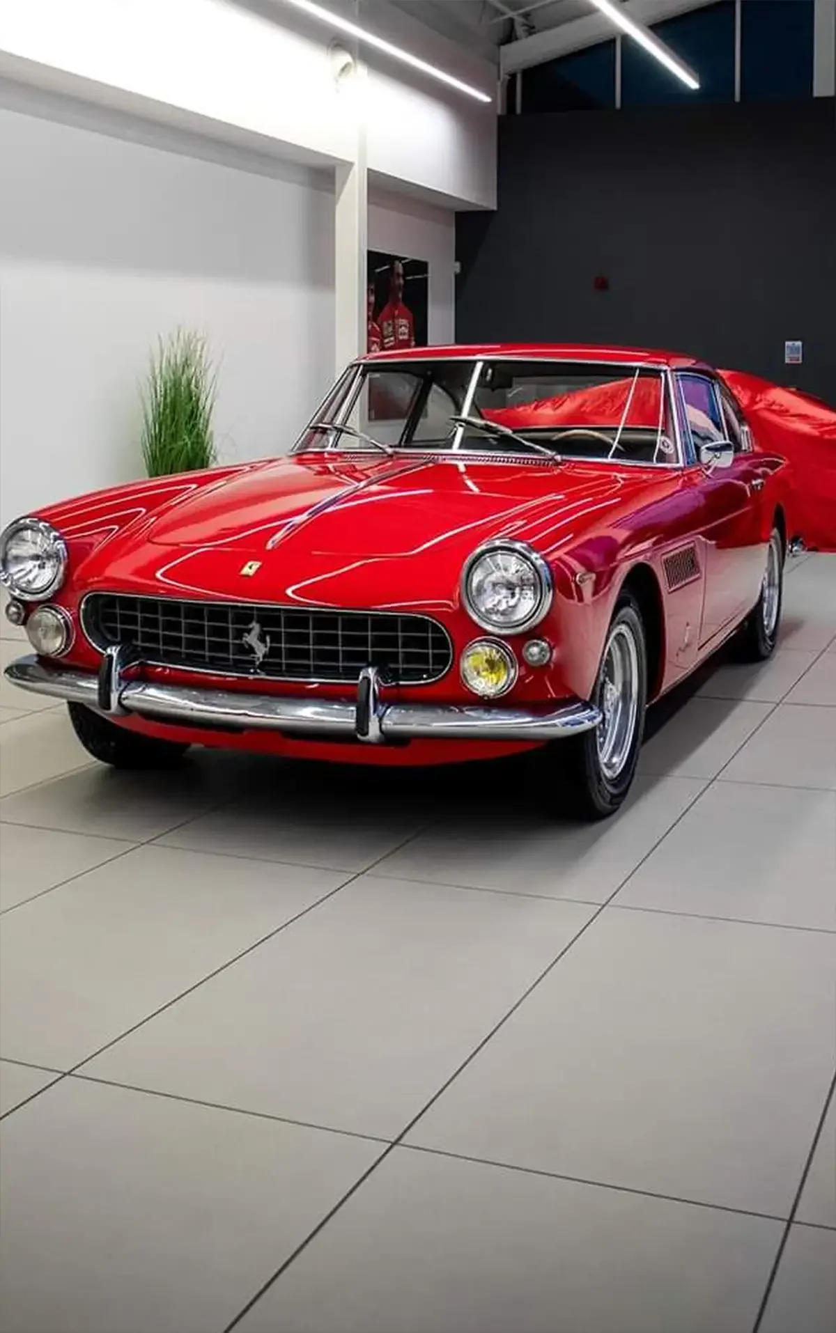 A classic red car with a shiny chrome grille and round headlights is parked indoors on a tiled floor. 