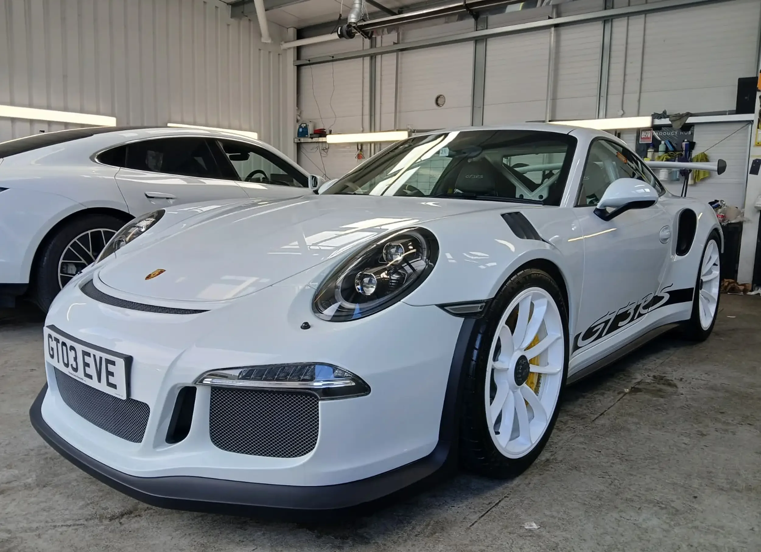A sleek white sports car, a Porsche GT3, is parked in a well-lit garage. 