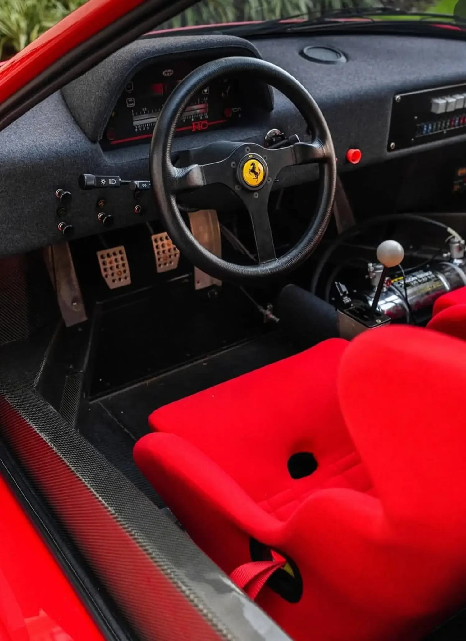 Close-up of a sports car interior with a black steering wheel featuring a yellow logo, bright red racing seat, and a manual gear shifter.