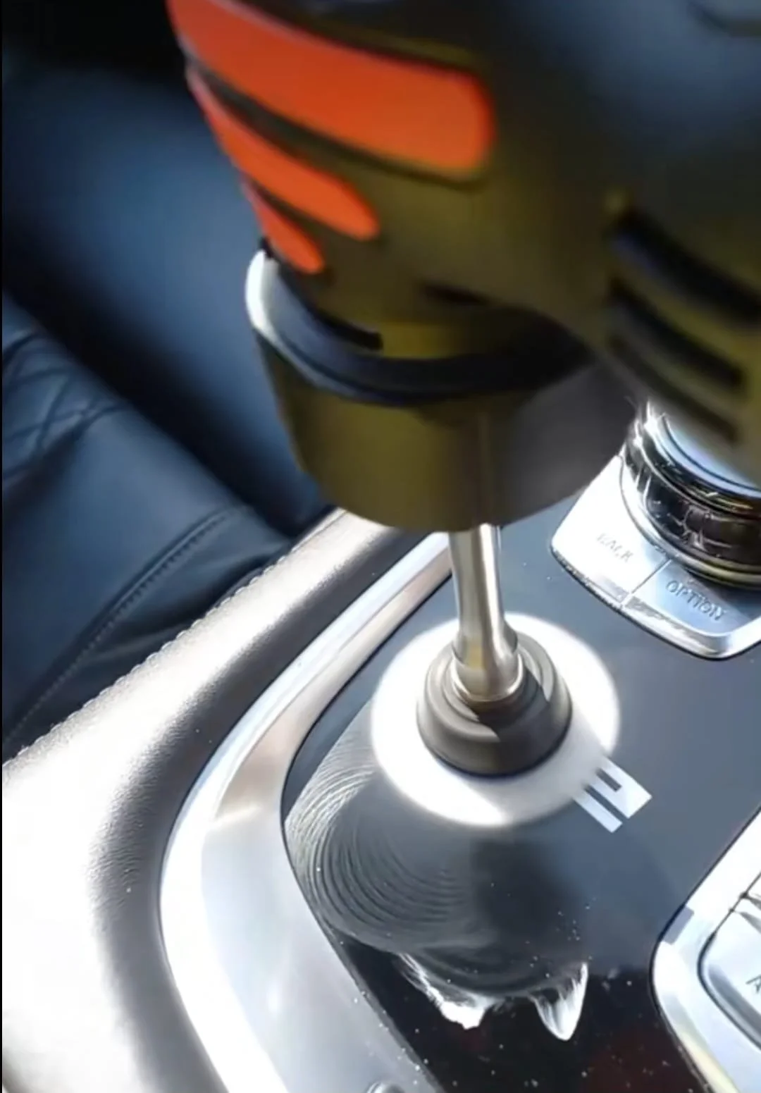 A close-up of a power drill being used to polish or modify a car's gear shift area. The drill is pressed against the surface, creating a shiny, glinting effect.