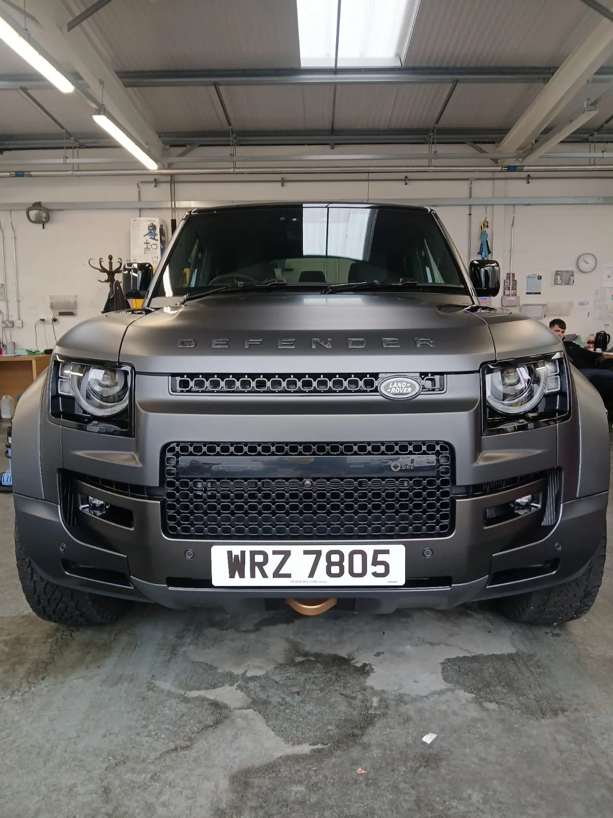 Front view of a black Land Rover Defender parked in a garage with industrial lighting, conveying a rugged and robust appearance