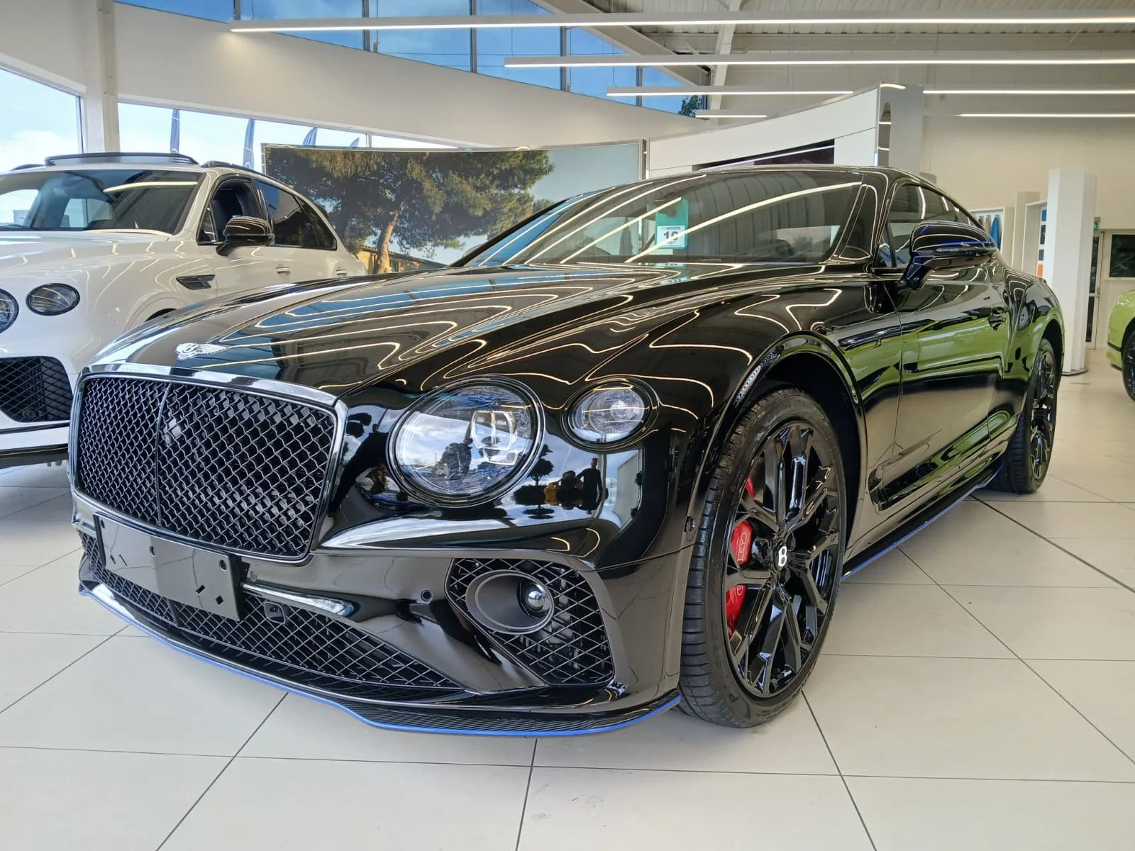 Sleek black luxury car with shiny chrome details and red brake calipers, displayed in a showroom next to a white car